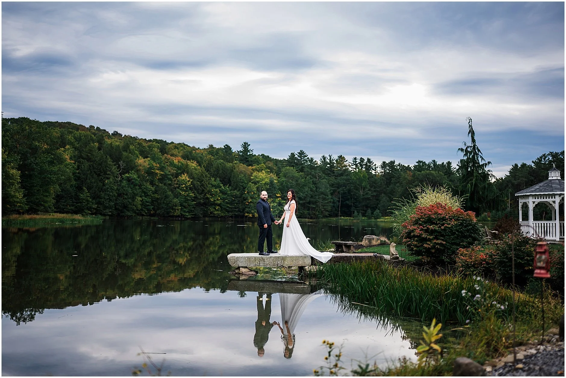 Newlyweds holding hands at the lake with their reflection showing in the water