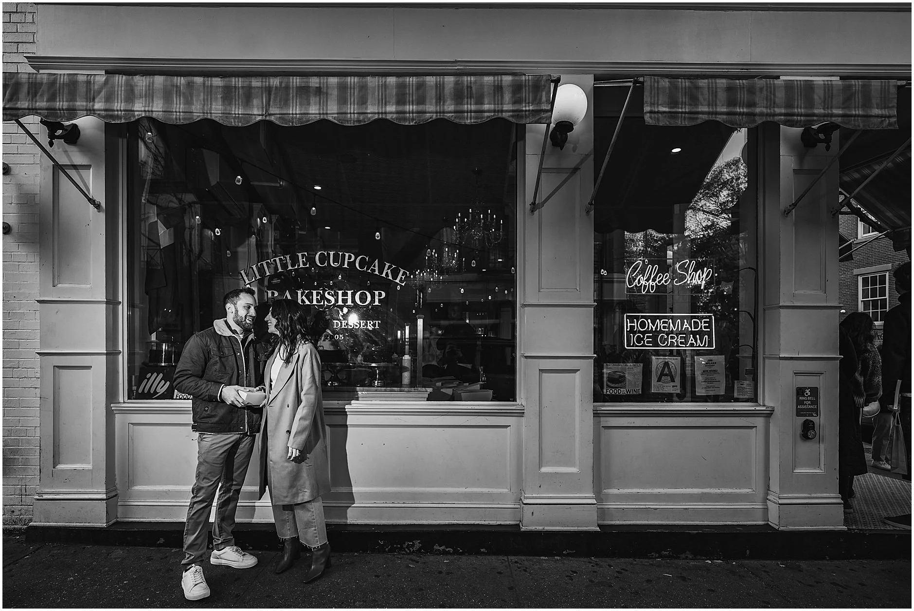 Black and white candid image of couple laughing as they stand in front of Little Cupcake Bakeshop in Soho