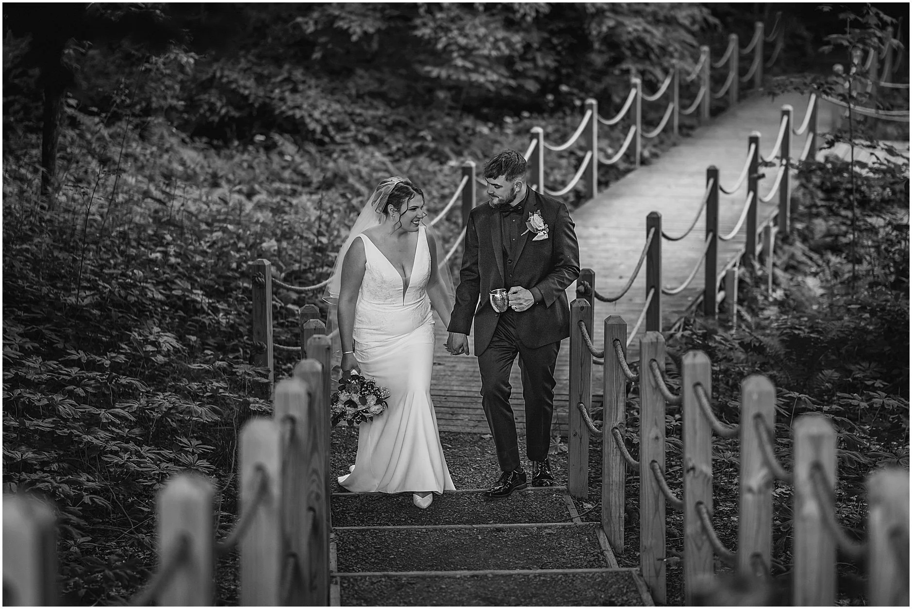 Black and white photograph of a bride and groom walking up a set of stairs in the woods after their ceremony in the Catskills, New York.