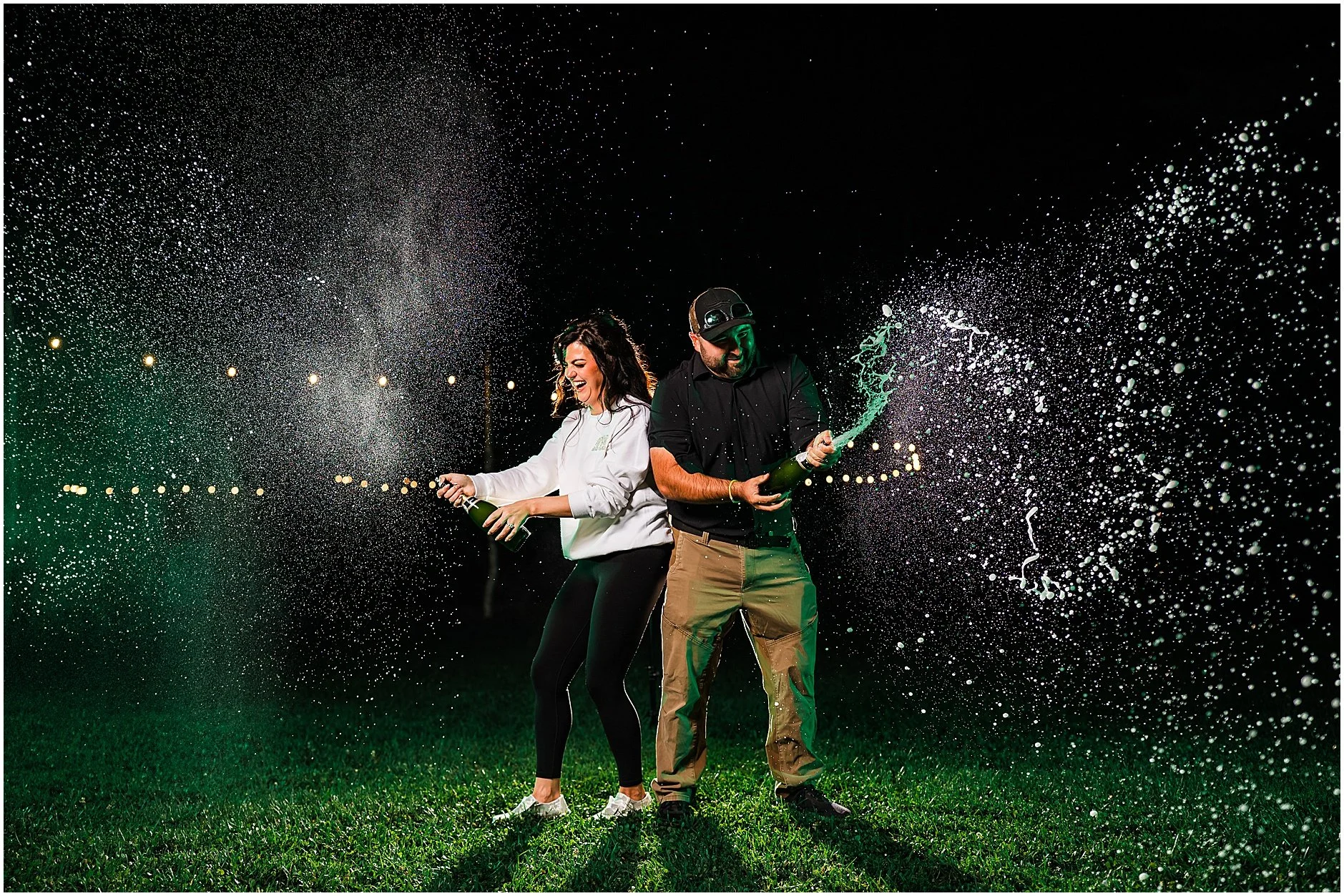 Newlyweds popping champagne in the dark by the camp fire at The Rosemary at Spano Lake in Upstate New York
