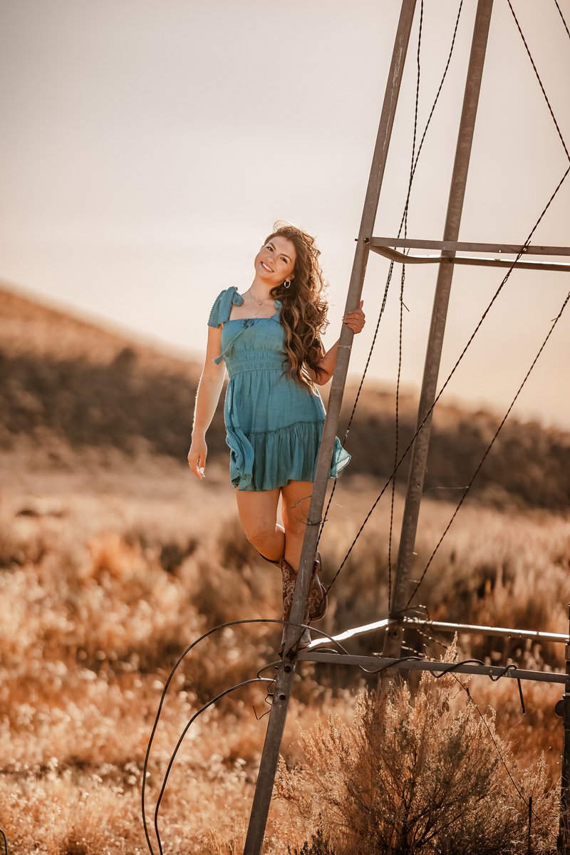 A woman in a blue dress standing outdoors near a metal structure in a sunlit field.