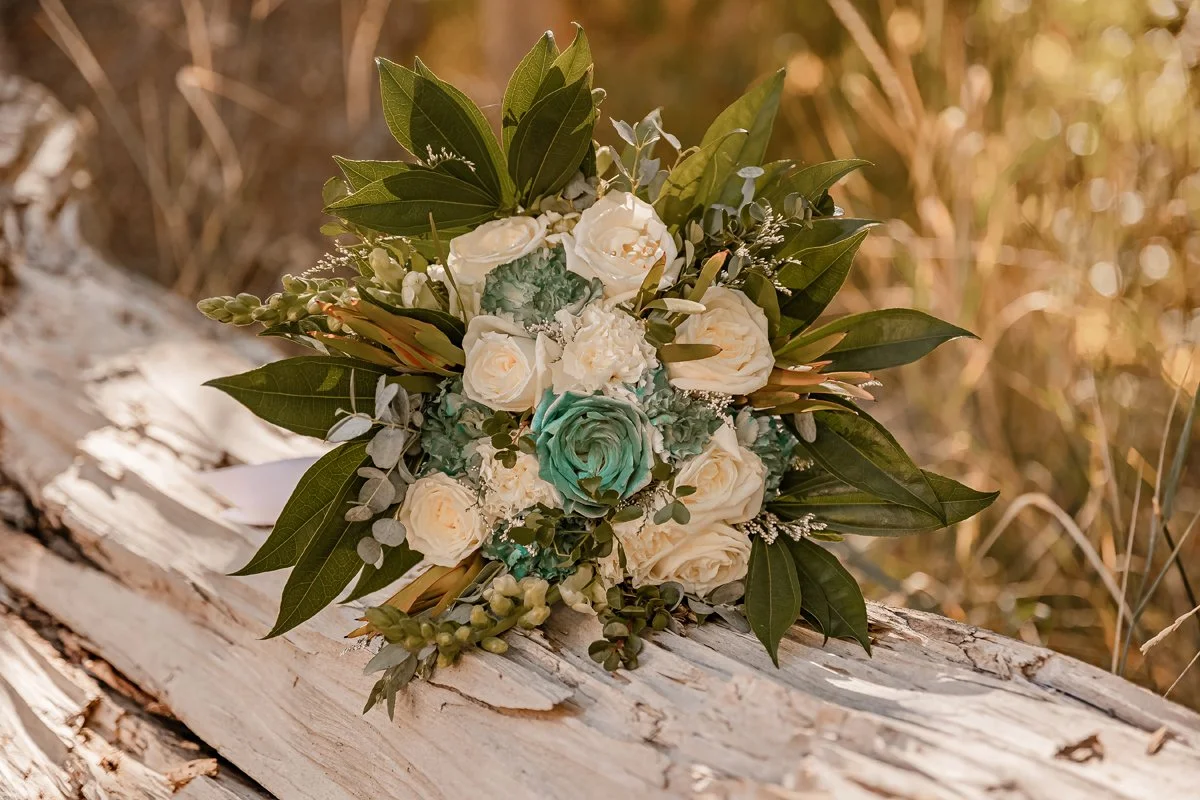 A bouquet of white and green flowers resting on a weathered wooden log in an outdoor setting.