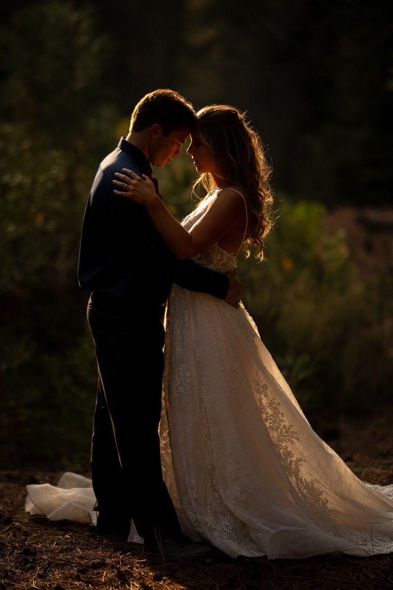 A couple dressed in wedding attire embracing outdoors at sunset.