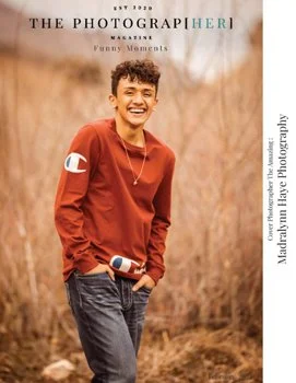 Young man in red sweatshirt smiling, standing outdoors in a natural setting, holding his hand in his pocket.