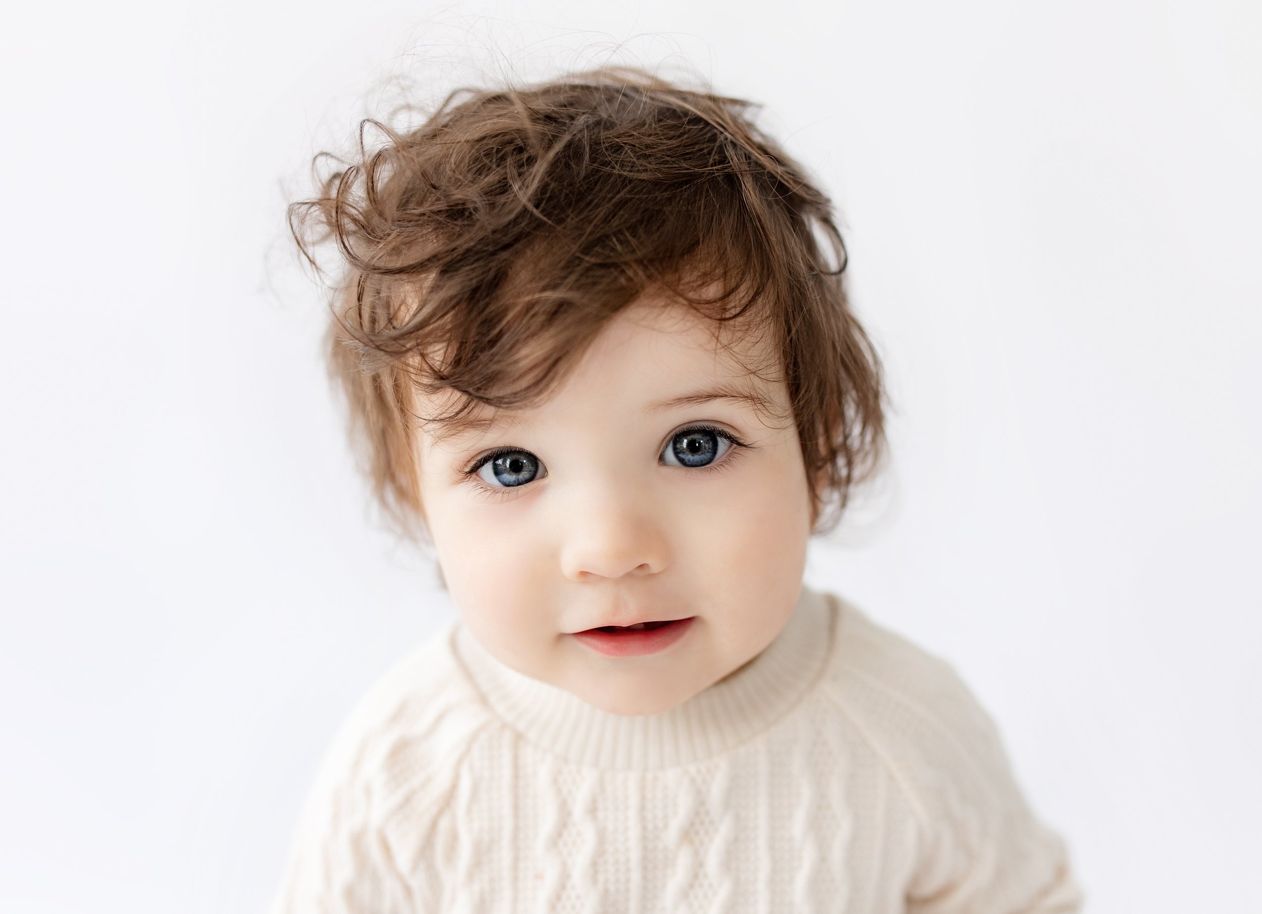 Milestone portrait with bright blue eyes and curly brown hair wearing a cozy cream sweater.