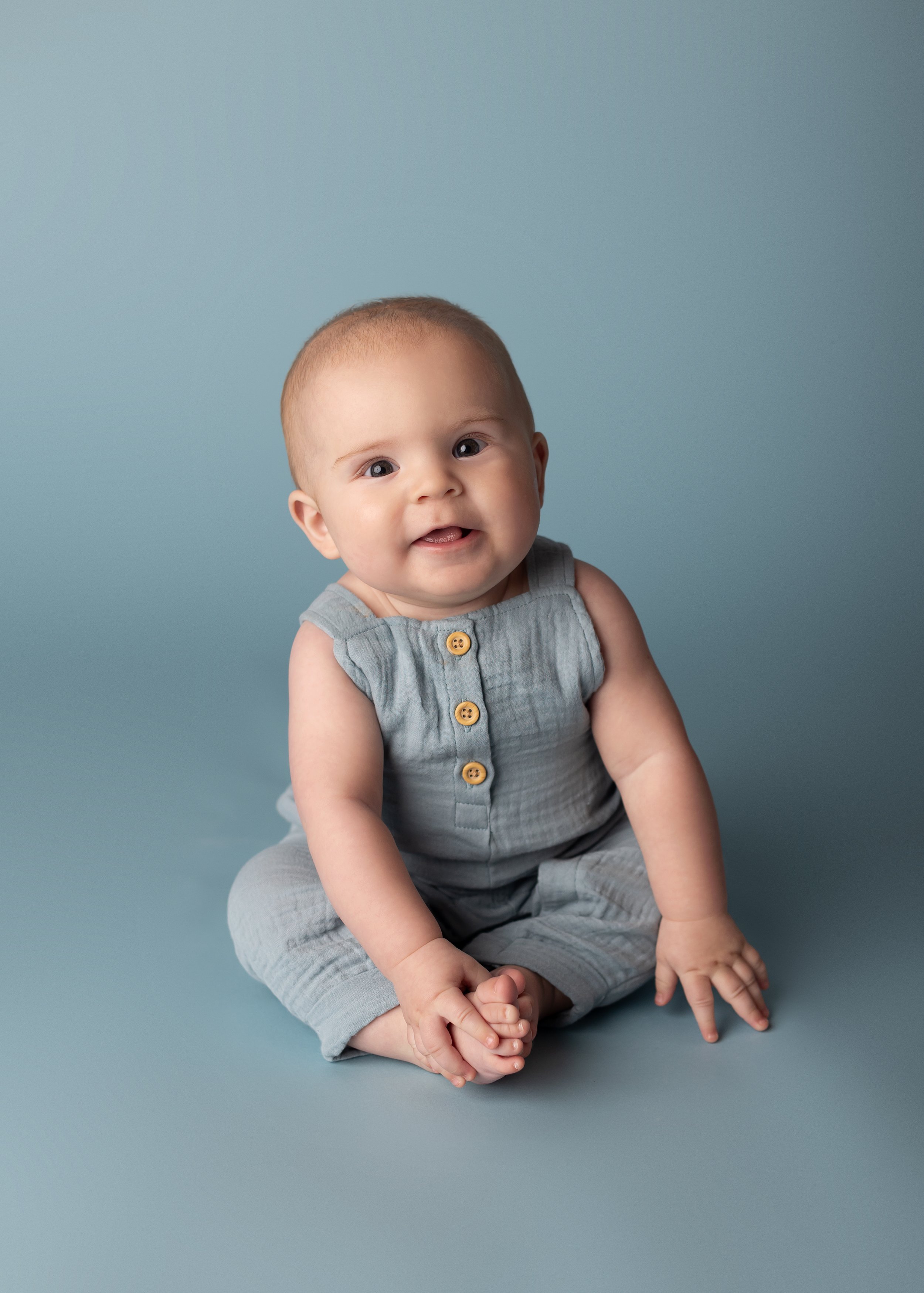 smiling baby sitting on a blue backdrop during a milestone photo session.