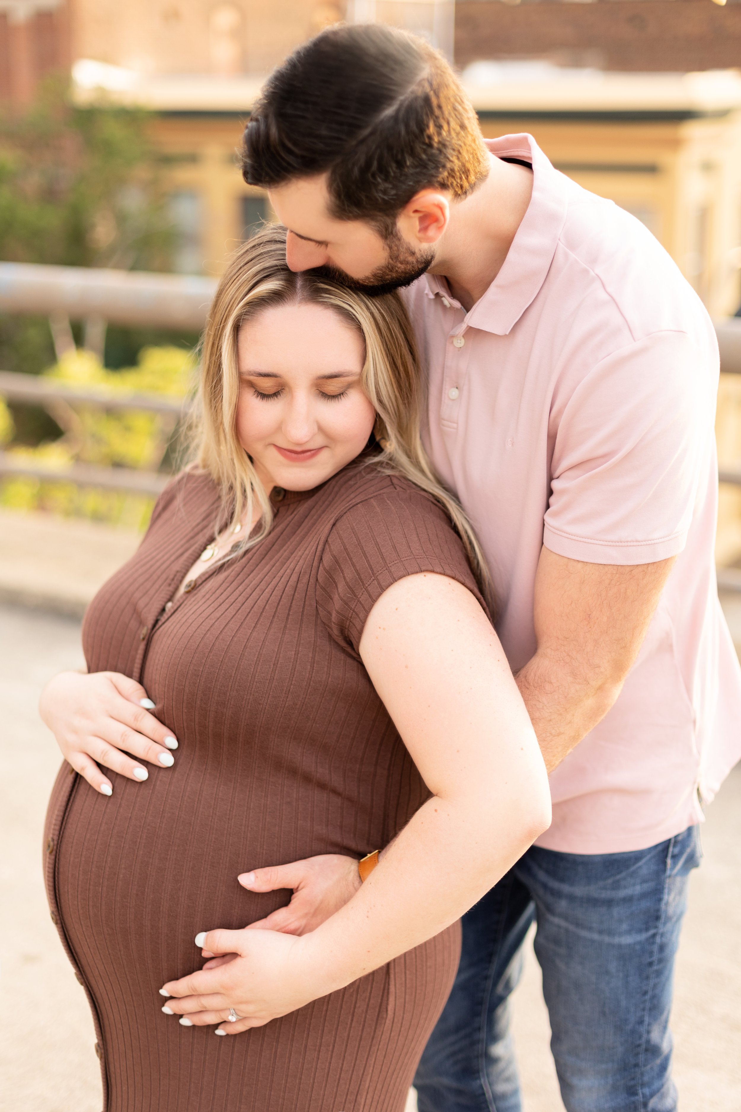 Heartwarming maternity photo of an expecting couple embracing, capturing a joyful moment of connection with golden lighting on a rooftop.