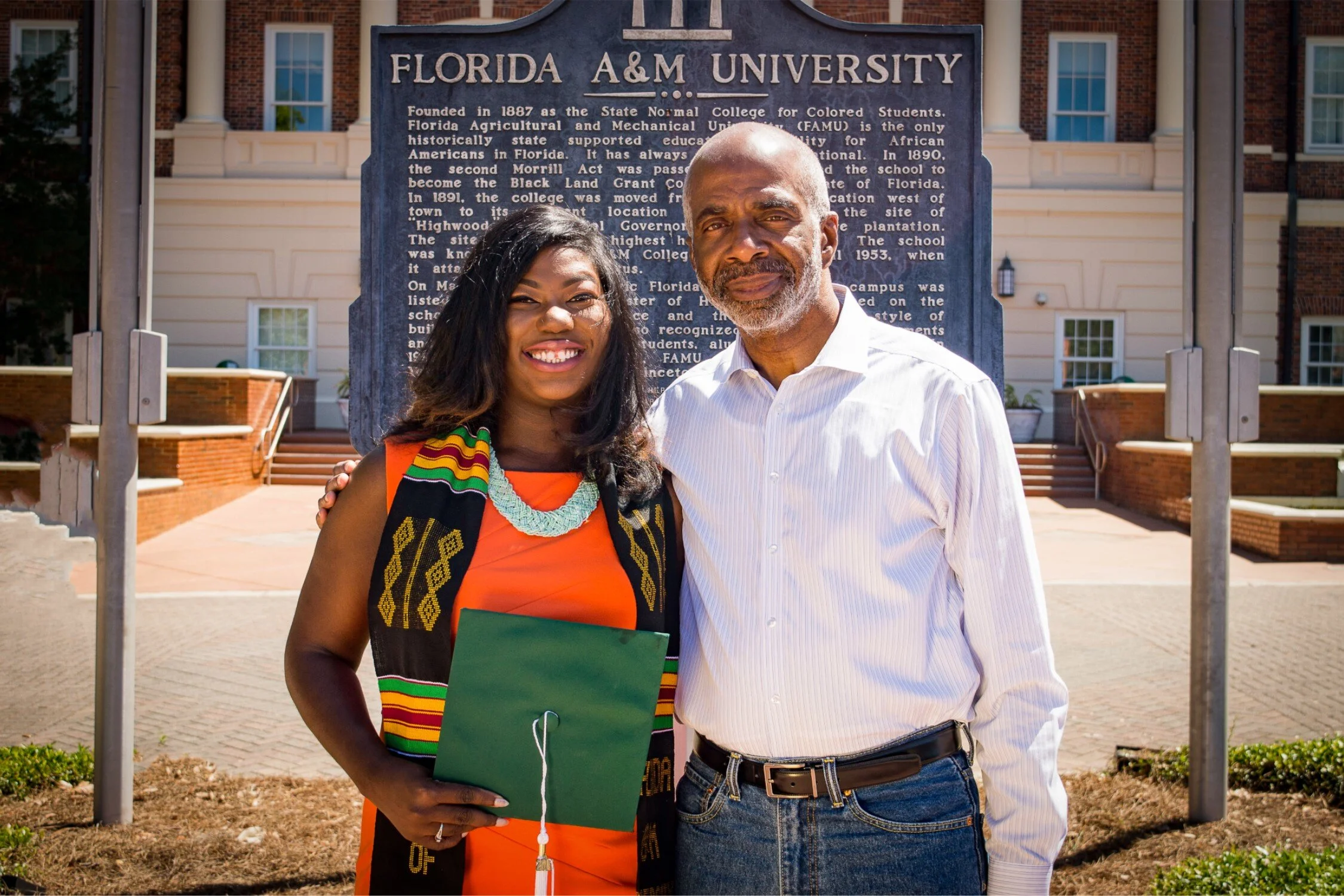 FAMU graduate Shaperlya posing with university president in an orange dress and graduate stole