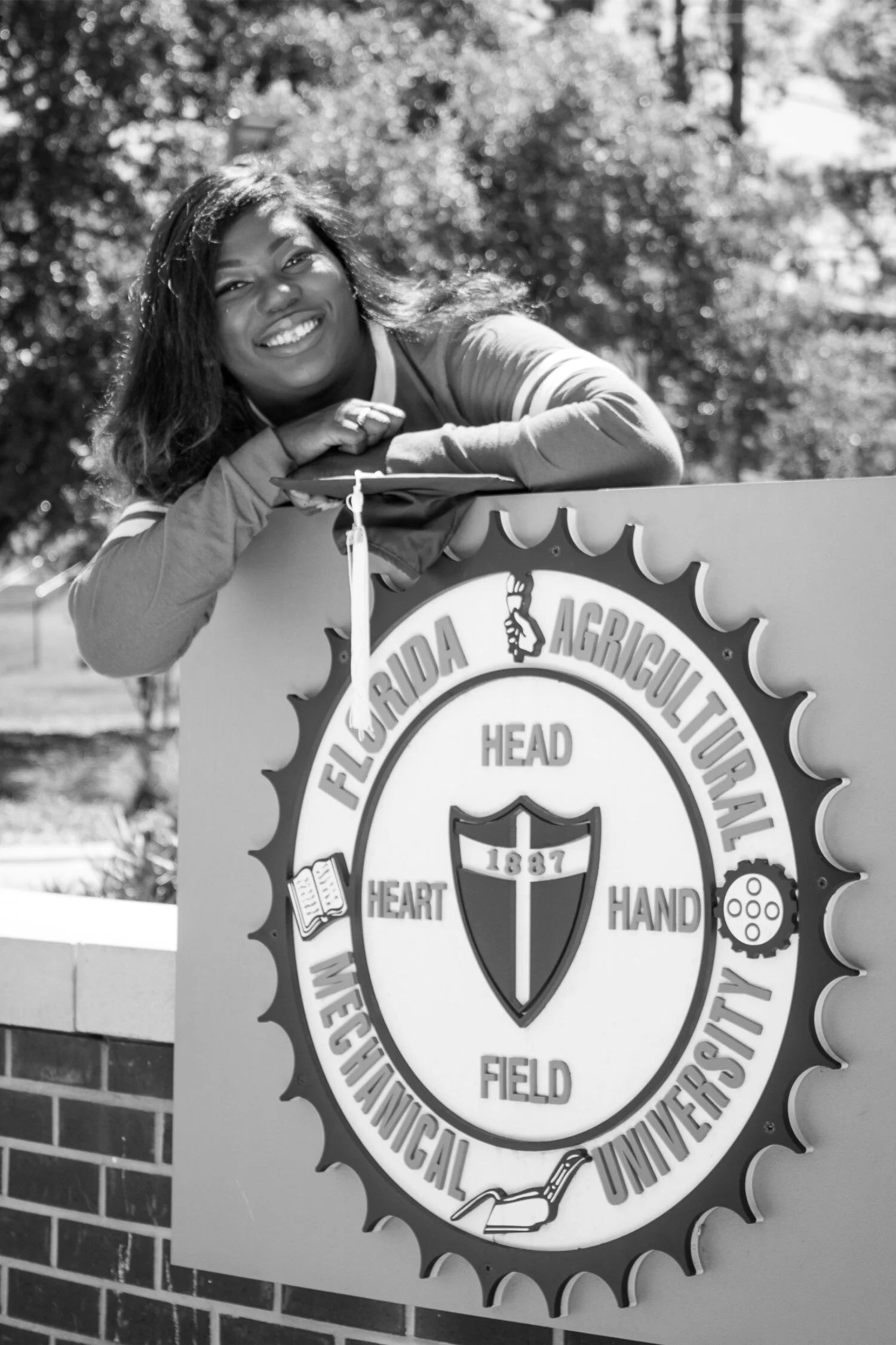  Black and white photo of graduate Shaperlya posing on new FAMU roundabout in a casual university tshirt and jeans. 