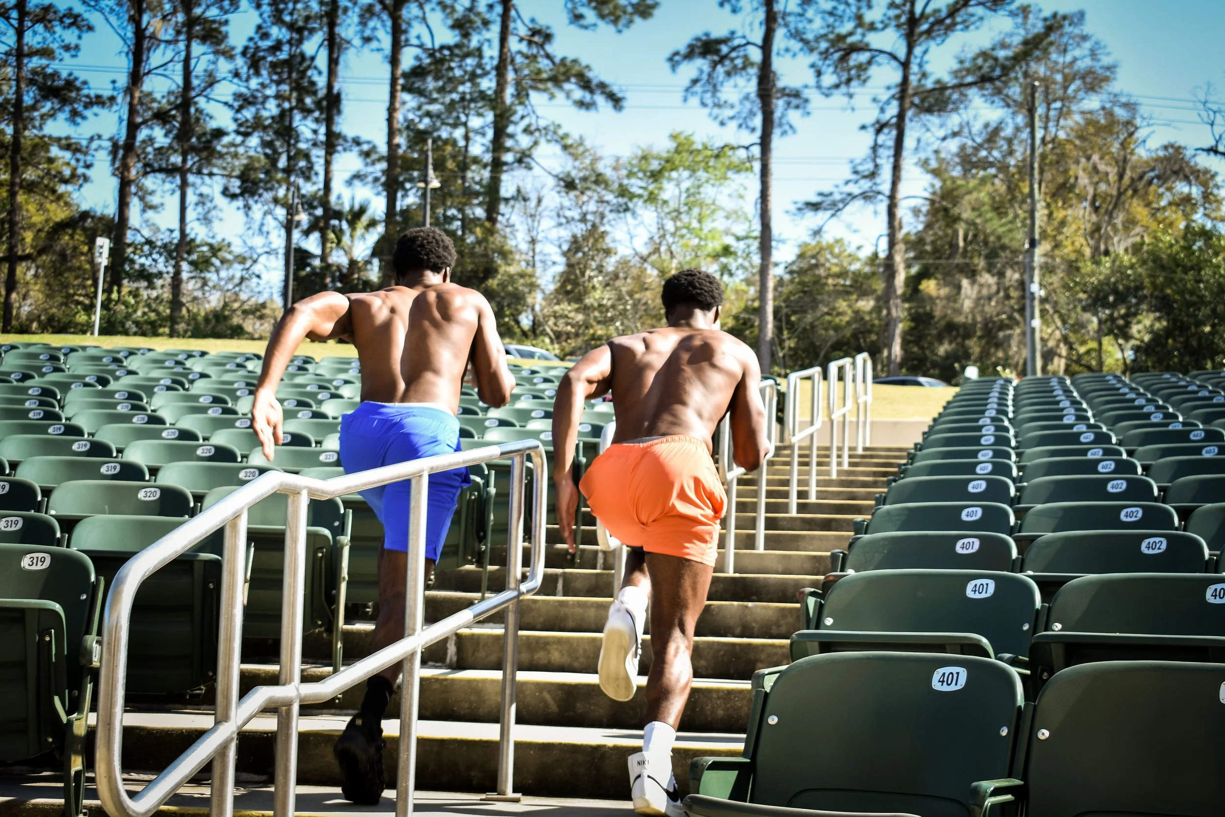 A personal trainer runs with his client up some stadium seating for an outdoor fitness photoshoot session.