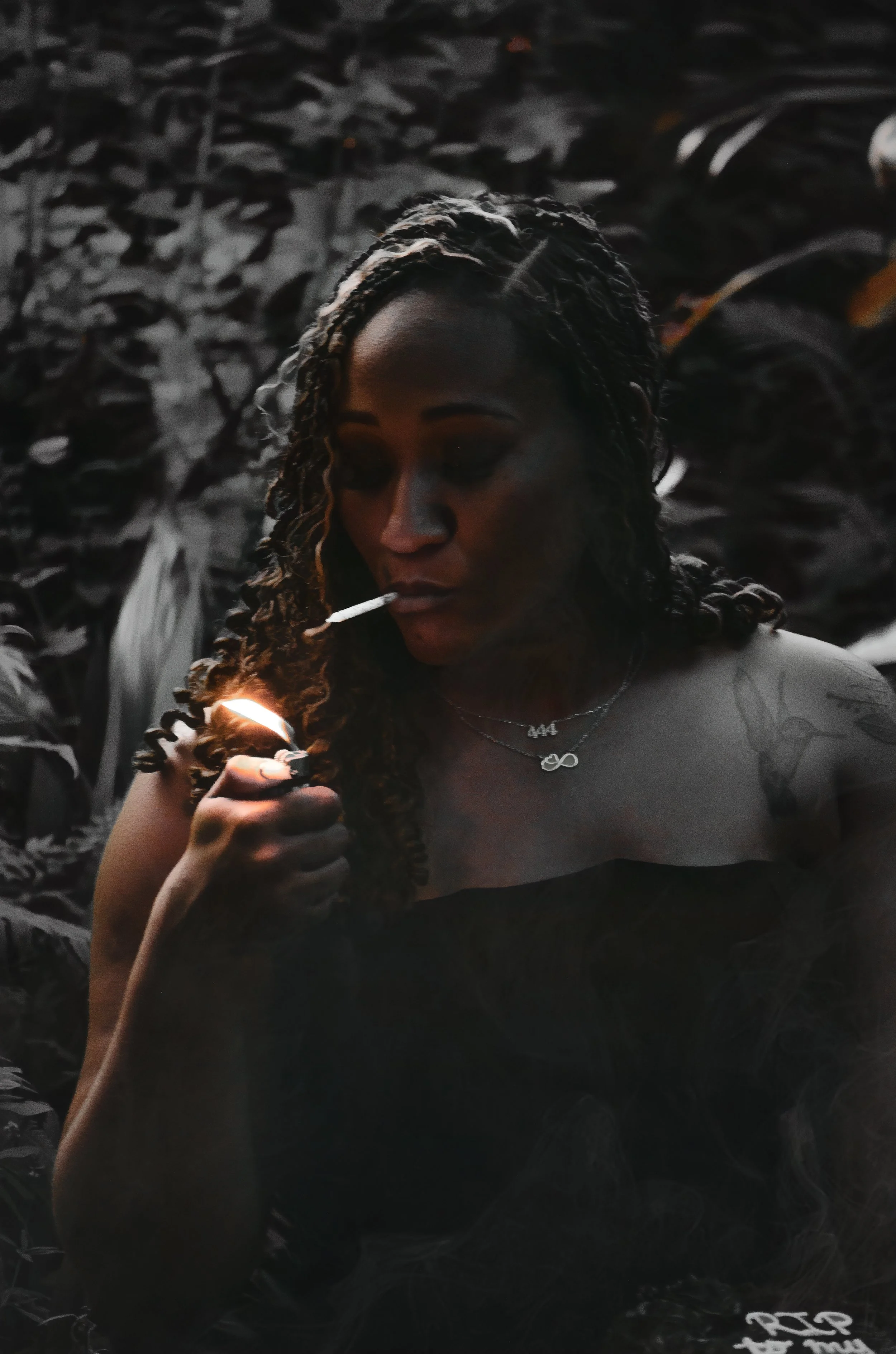 Muted color tone photo of a woman holding a candle in her lips and striking a lighter to ignite the candle. Woman holds a cake covered in black icing with the words "RIP to my 20's" in white icing.