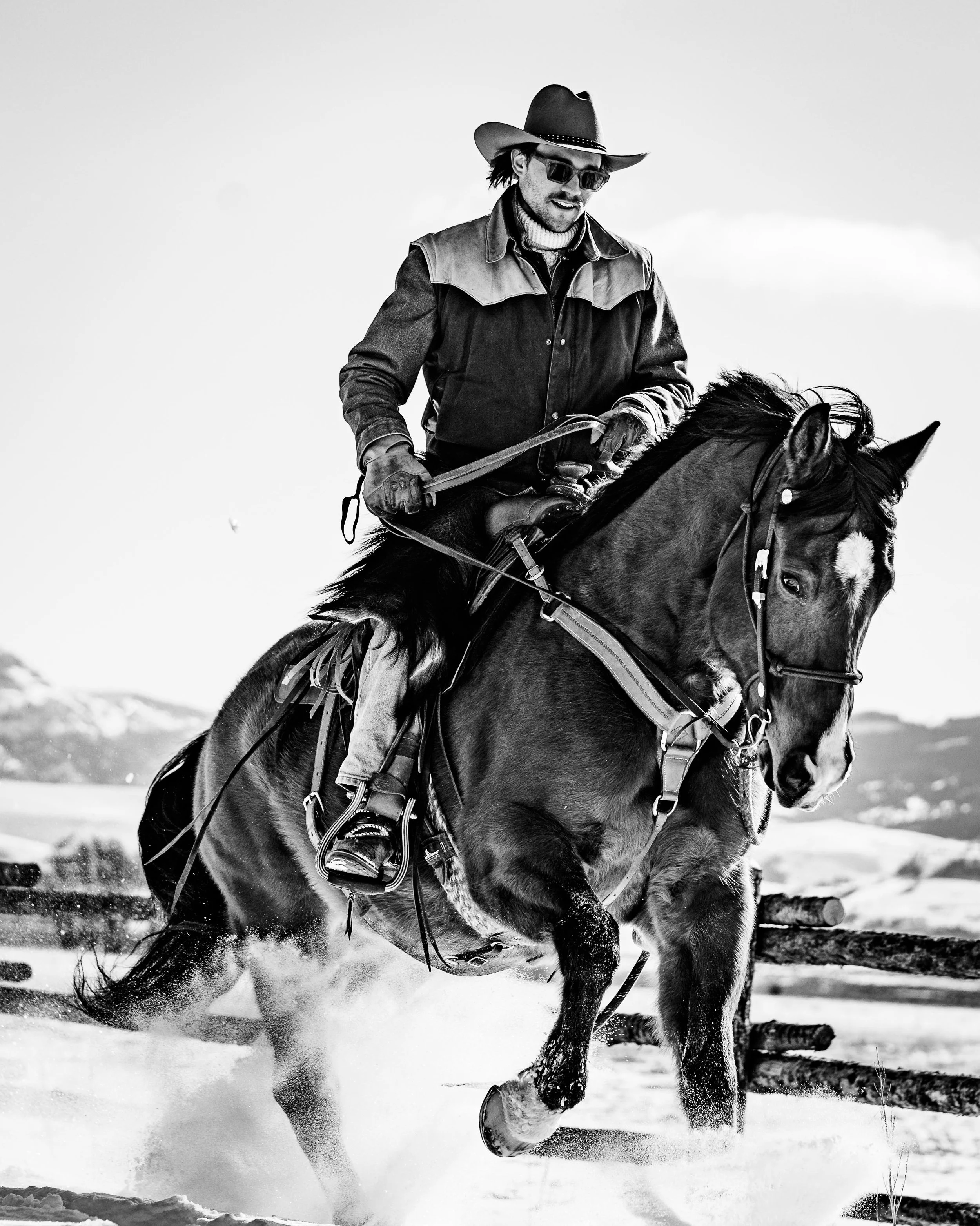 A man riding a horse in a snowy landscape, wearing a cowboy hat sunglasses, and outdoor clothing