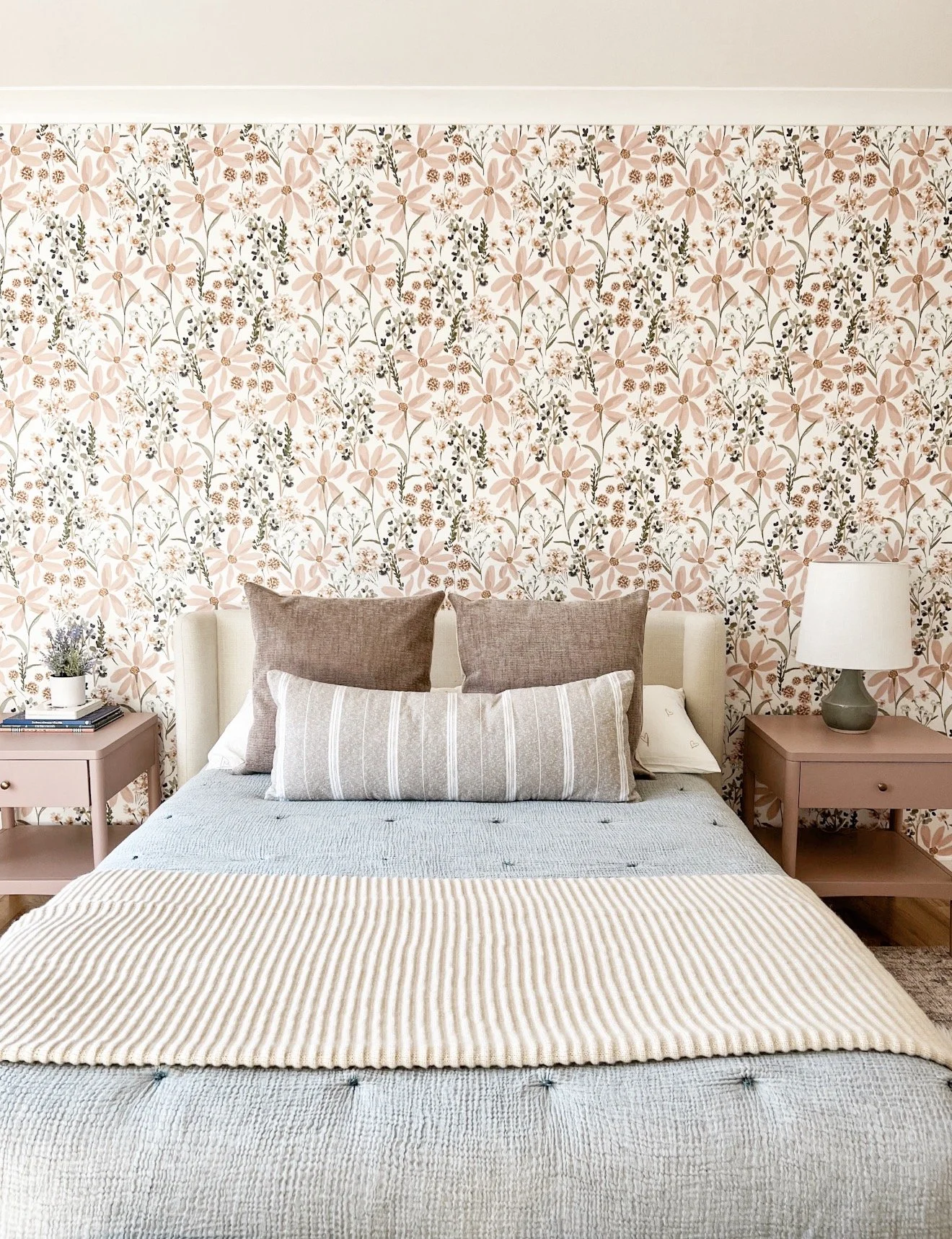 Bedroom with pink floral wallpaper, upholstered bed, and soft layered neutral bedding