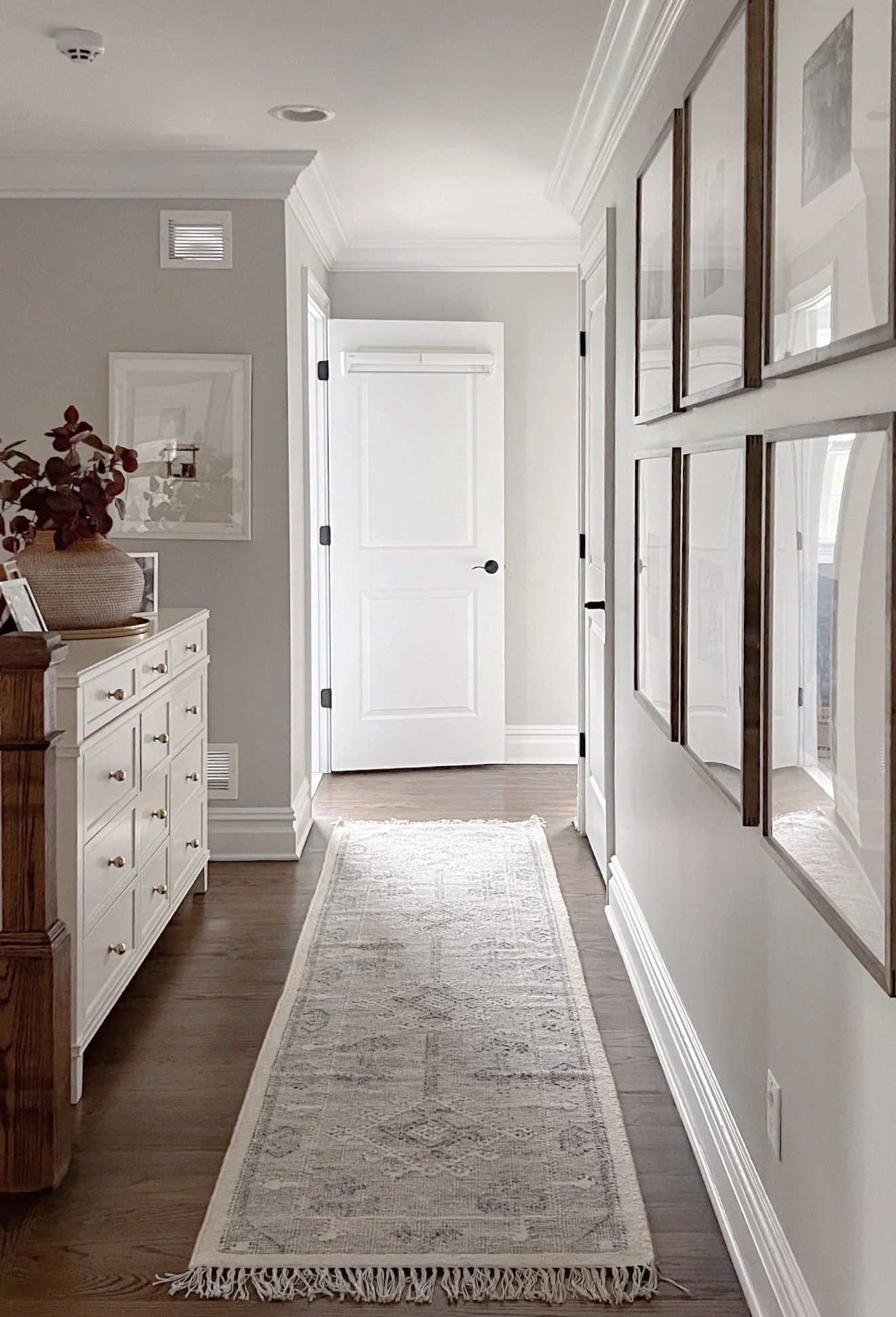 Long hallway with a neutral runner rug, hardwood floors, white walls, and natural light.