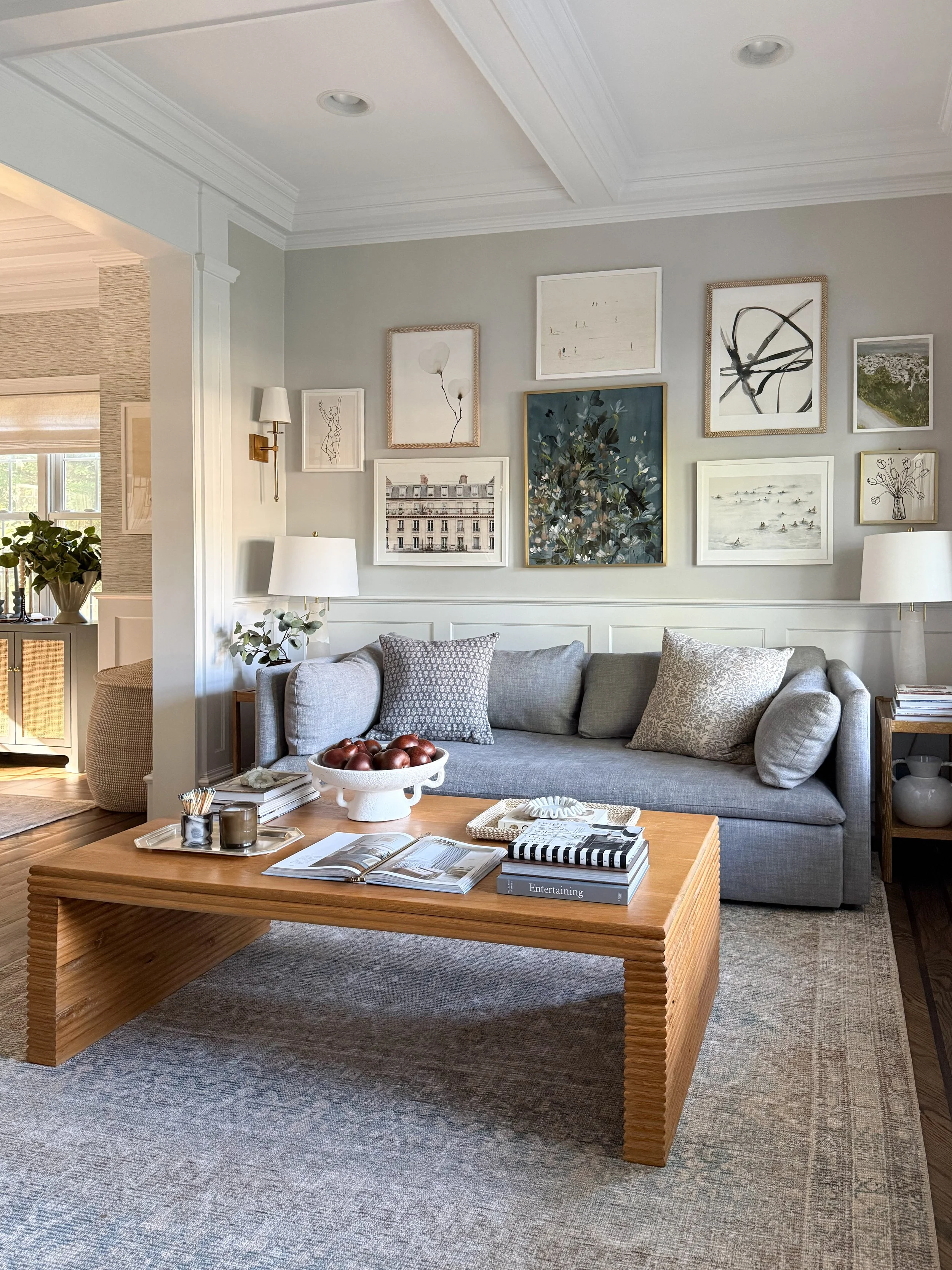 Cozy living room featuring a neutral patterned area rug, gray sofa, wood coffee table, and gallery wall.