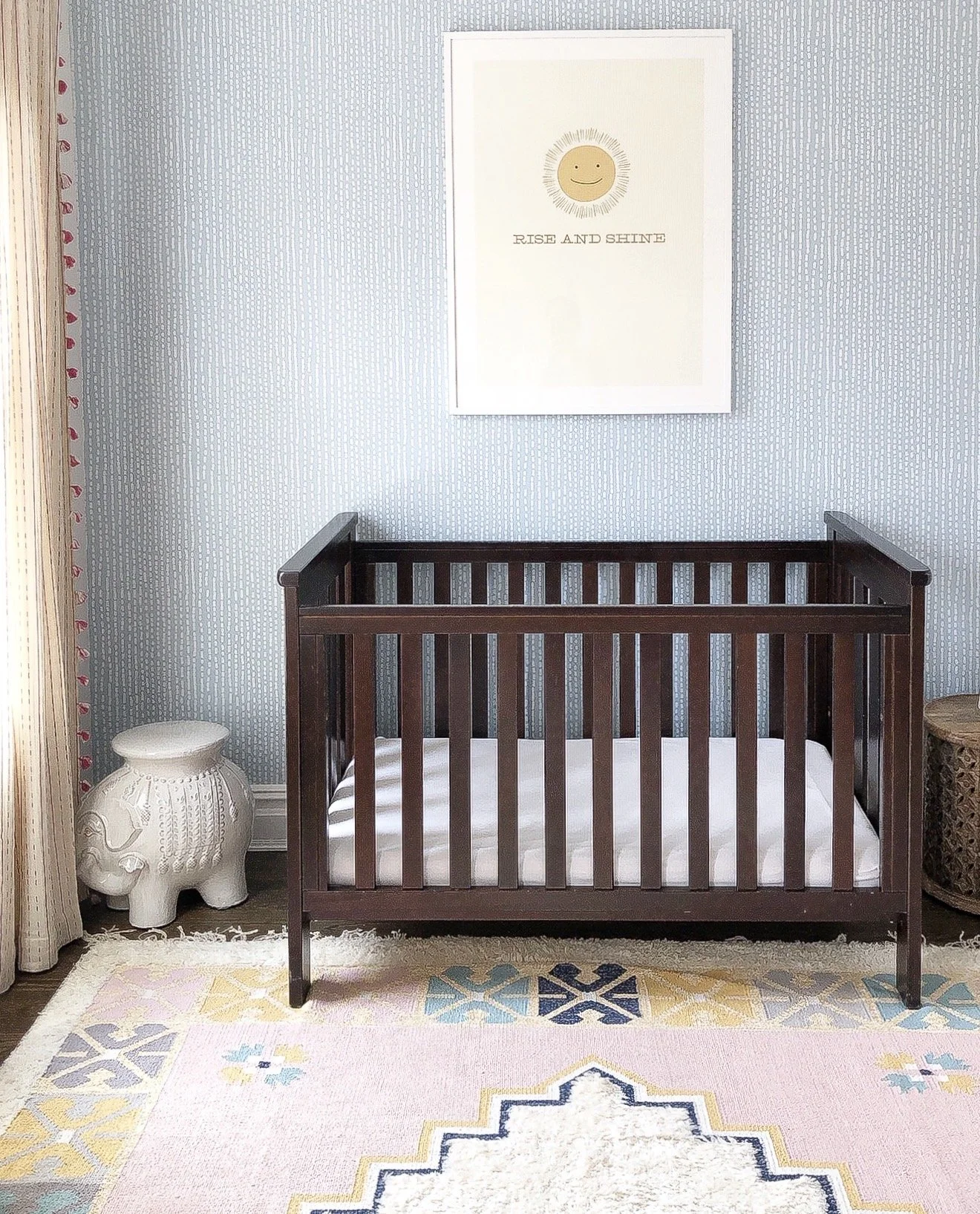 Neutral nursery with patterned wallpaper, dark wood crib, and colorful area rug