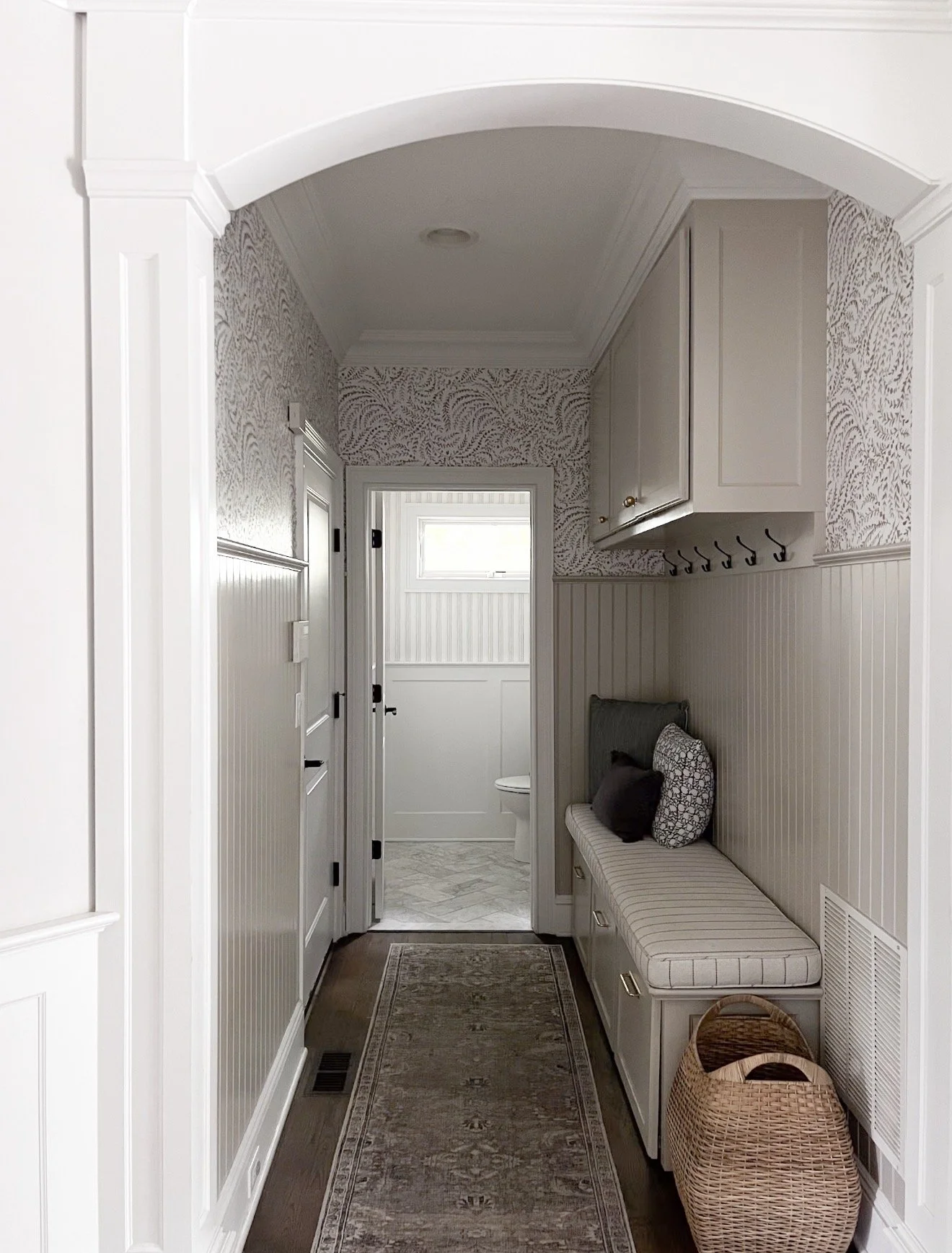 Mudroom hallway with beadboard painted Benjamin Moore Revere Pewter, neutral wallpaper, built in bench seating, and woven basket storage.