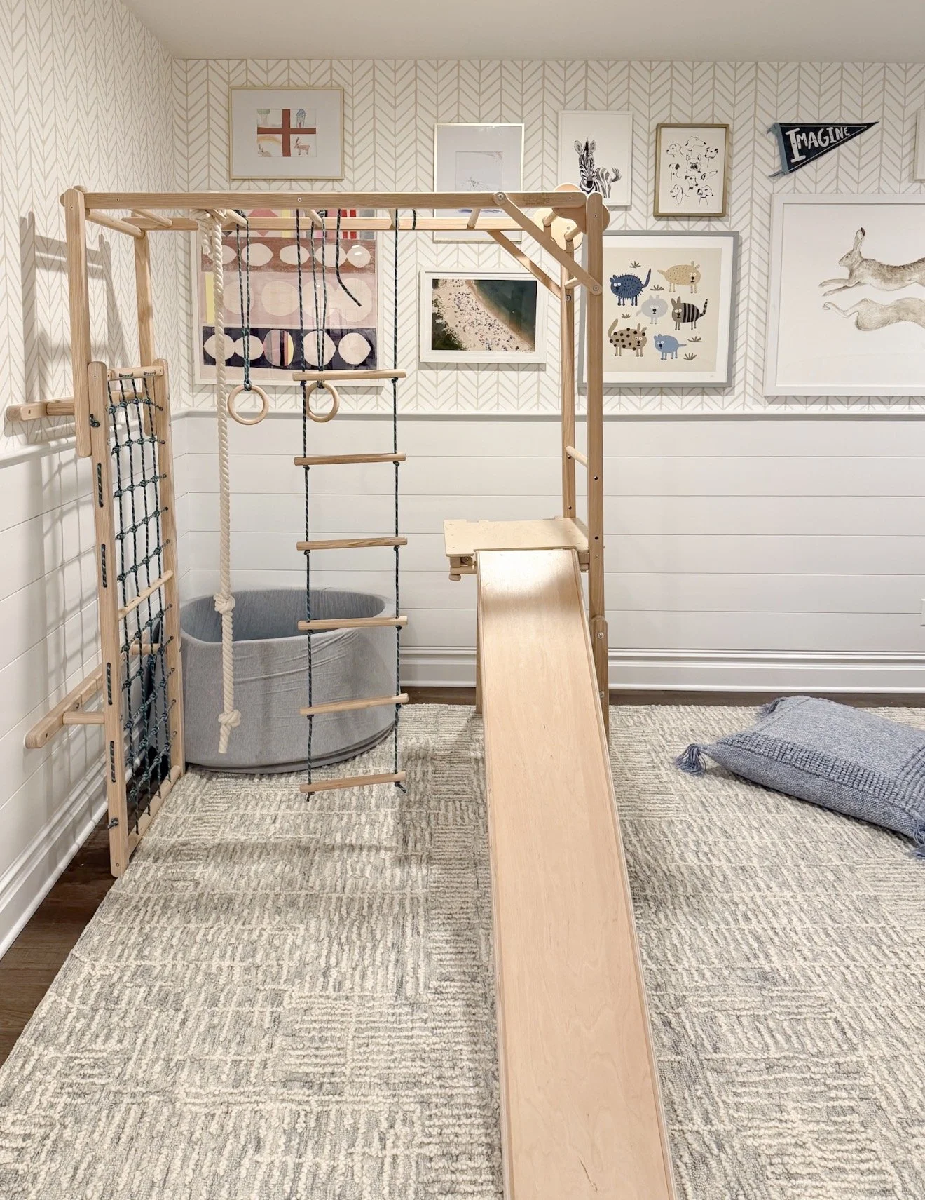 Kids’ playroom with a wooden indoor play gym, gallery wall, white paneling, and a light neutral geometric Loloi area rug.