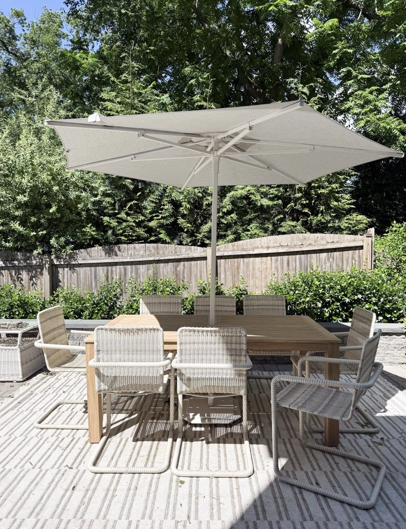 Outdoor dining area with a wood table, woven chairs, large umbrella, greenery, and a neutral striped Loloi outdoor rug.