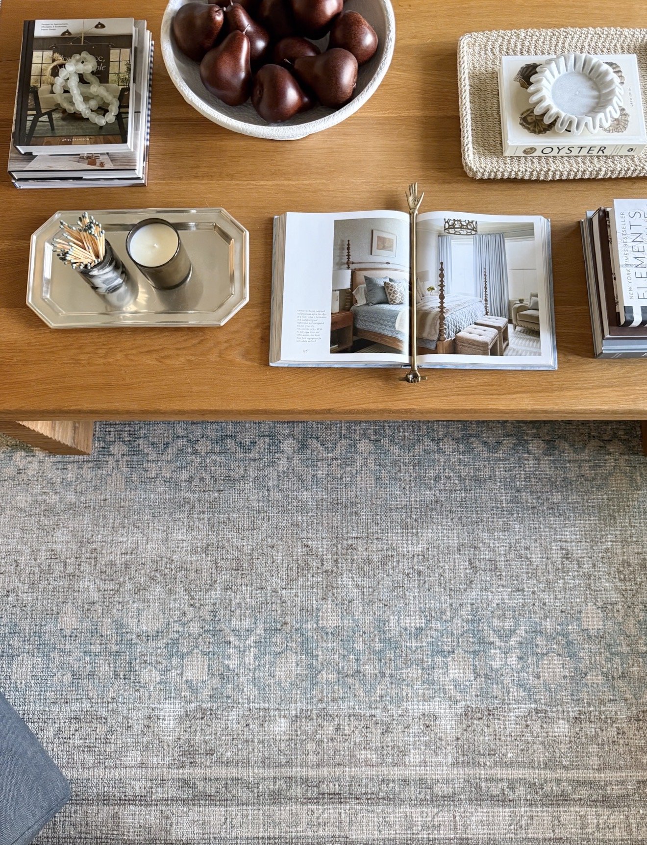 Overhead view of a living room coffee table styled with books, candle, decorative objects, and a softly patterned blue and neutral Loloi rug.