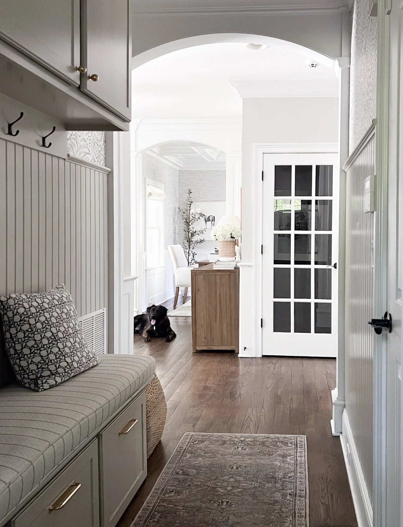 Bright mudroom hallway with built-in bench seating, patterned pillows, brass hardware, and a neutral vintage-inspired Loloi runner.