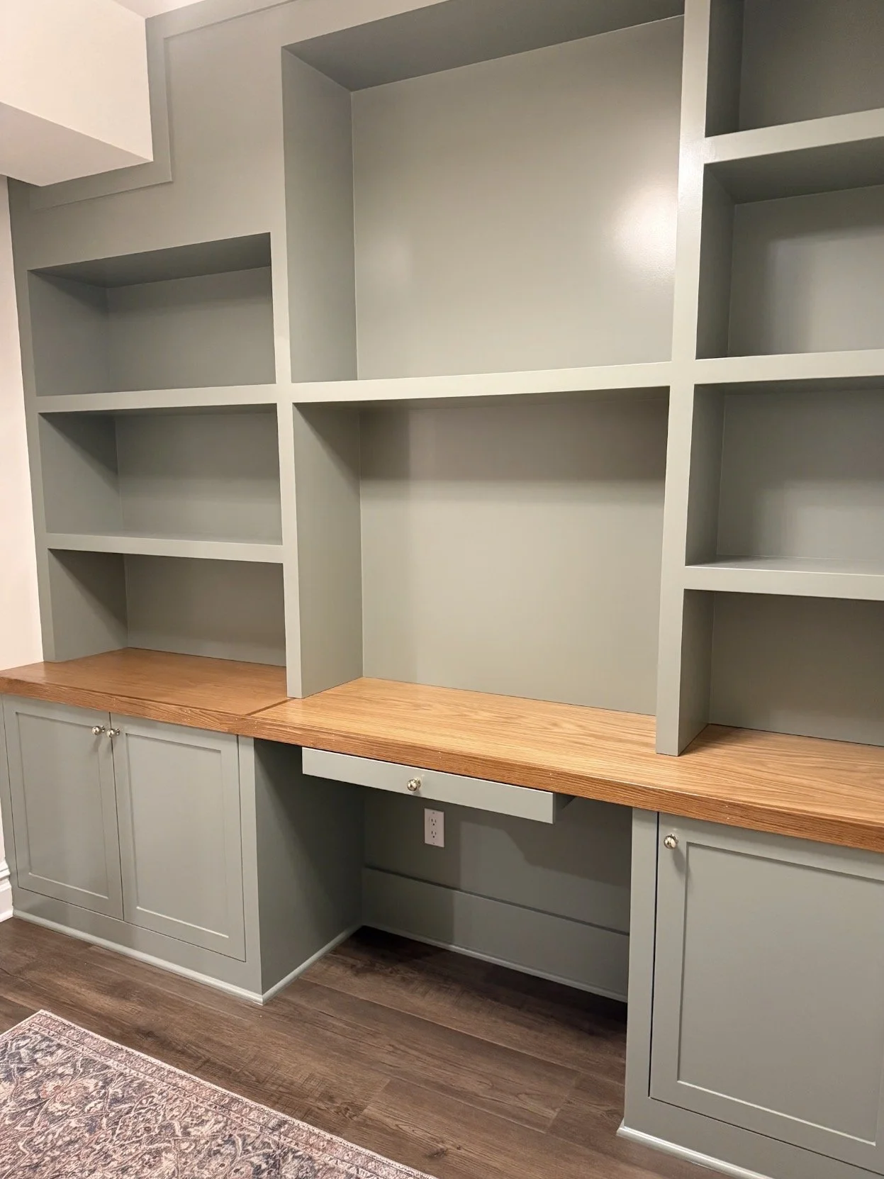 Basement built in shelving painted Sherwin Williams Evergreen Fog with wood desktop and cabinetry in a modern basement office workspace.