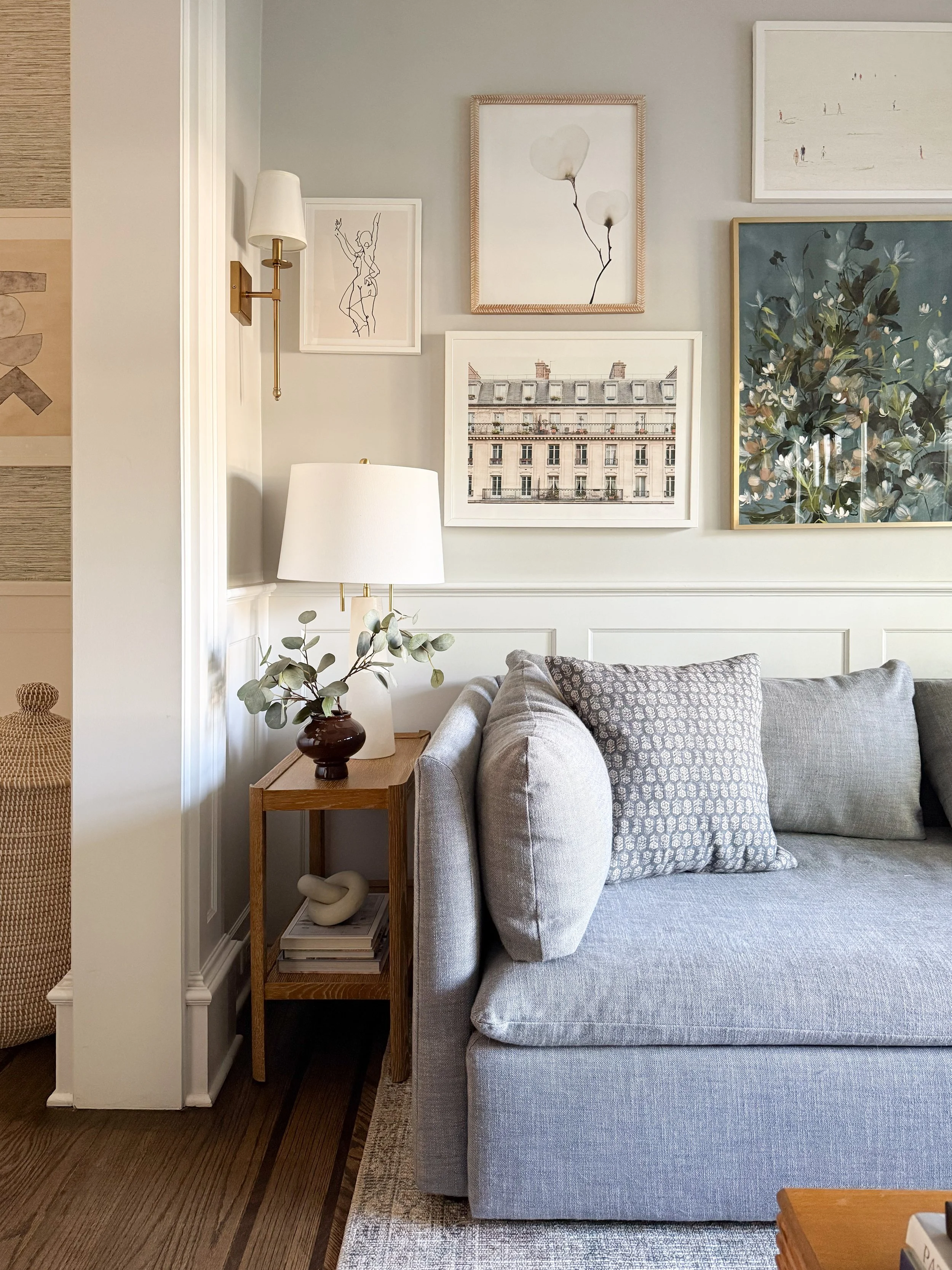 Cozy den with a brass wall sconce, gallery wall, and neutral sofa showcasing layered home lighting.