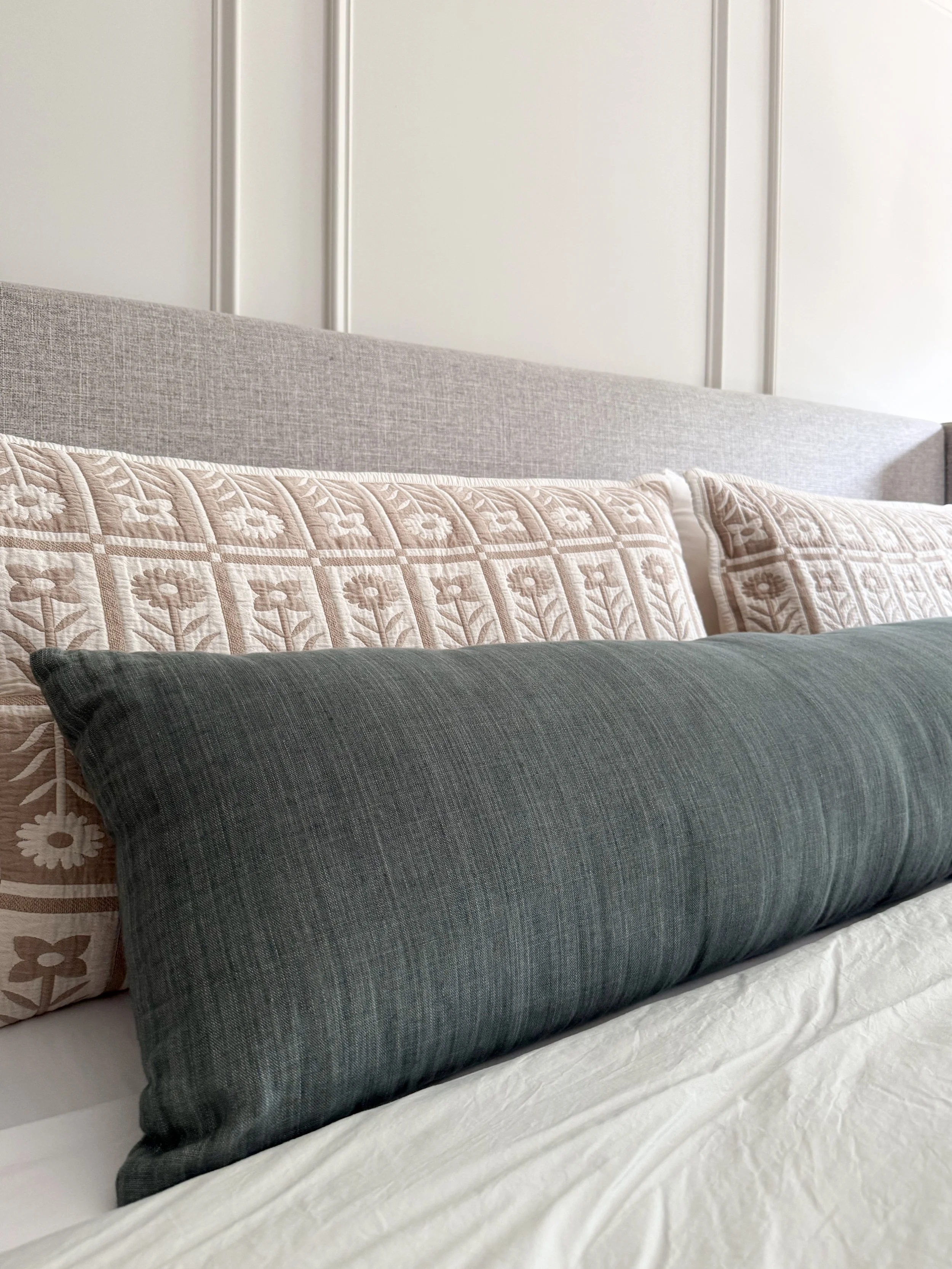 Close up of Quince floral quilted shams and decorative lumbar pillow layered on crisp white linen bedding.