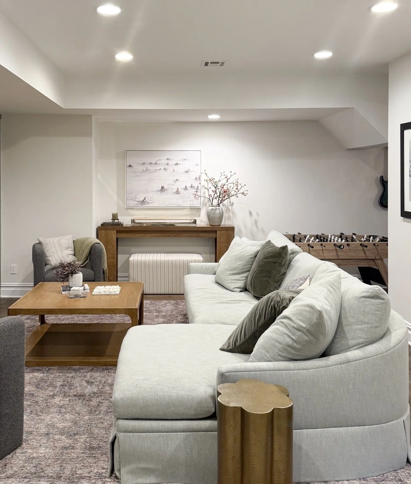 Basement family room with a large curved sectional, wood coffee table, layered neutral decor, and a muted Loloi area rug.