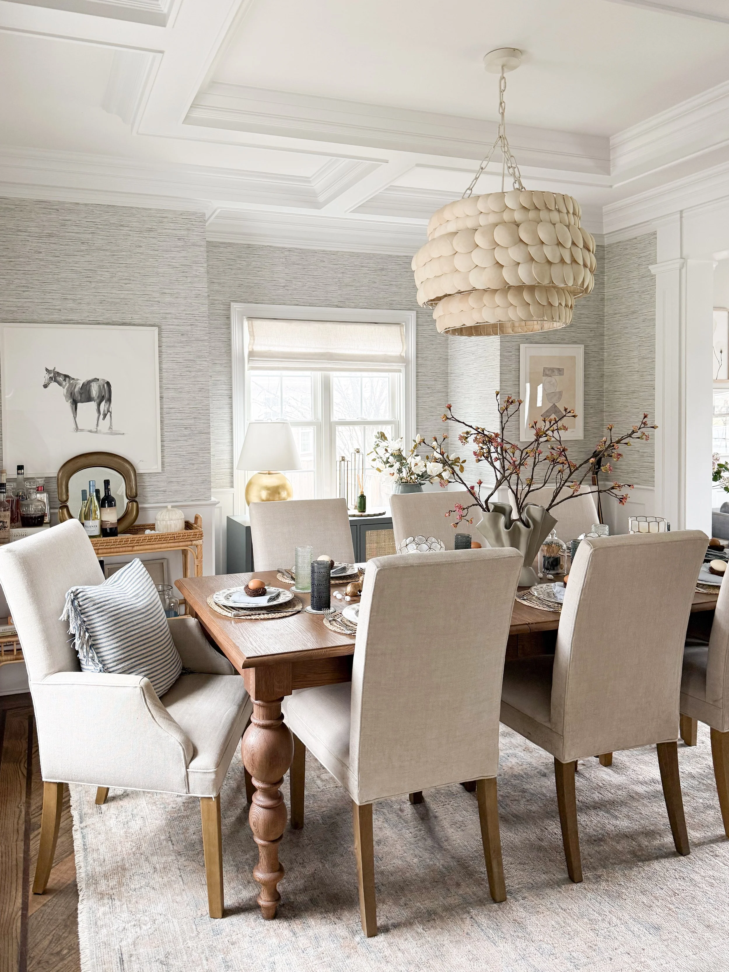 Dining room with a statement shell chandelier above a wood dining table in a neutral, modern home.