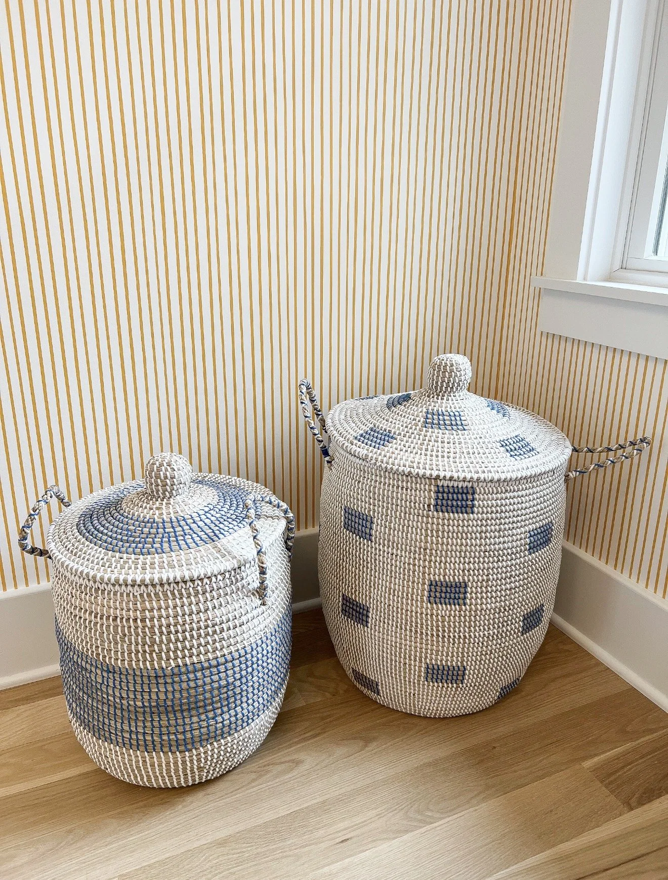 Reading nook with orange and white striped wallpaper, colorful children’s books, large windows, and blue patterned woven baskets.
