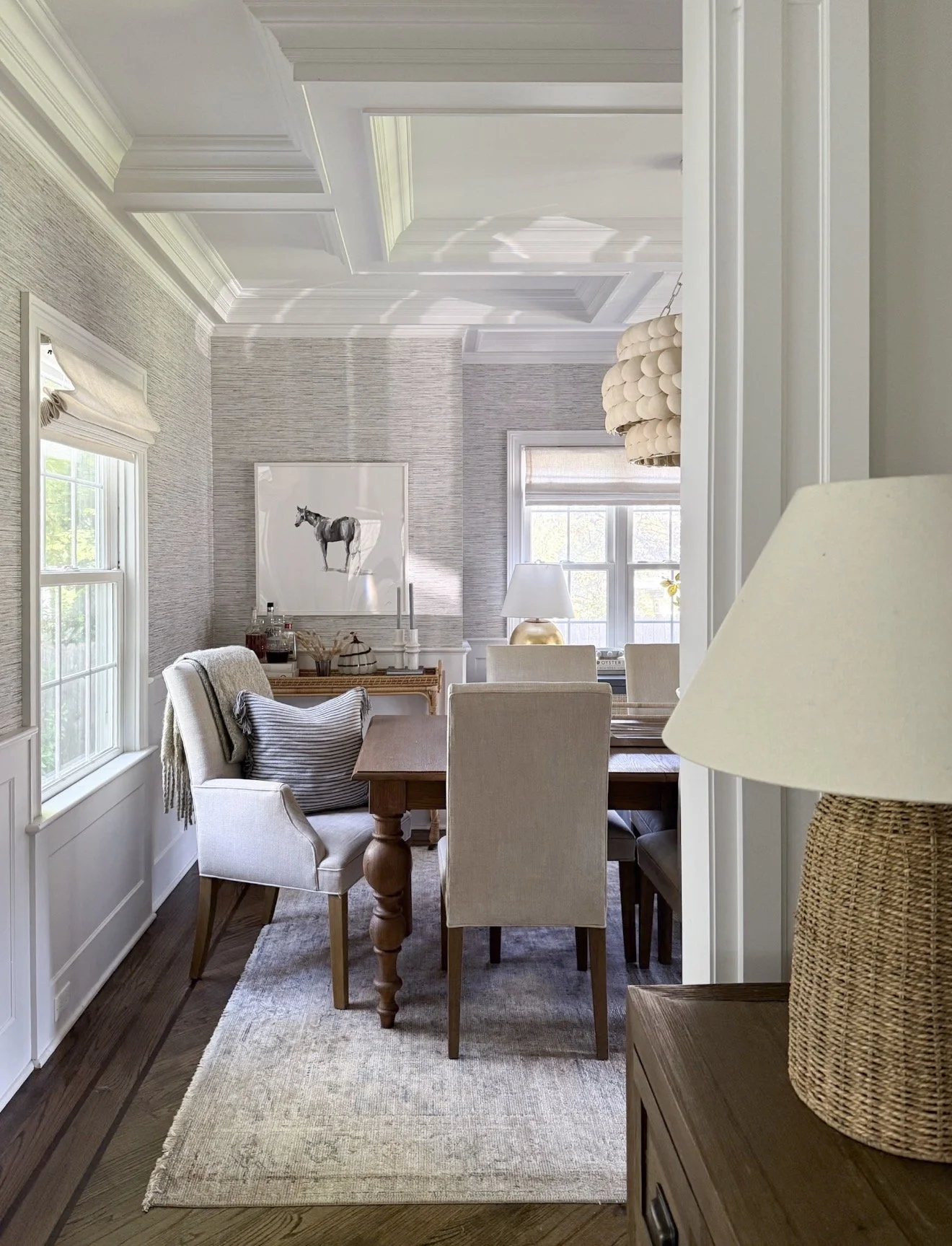 Neutral dining room with upholstered chairs, wood dining table, grasscloth walls, and a soft Loloi area rug beneath the table.