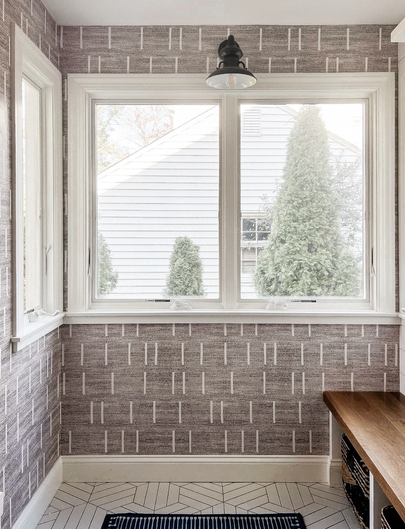 Close-up of gray geometric wallpaper layered with white patterned tile and a blue striped area rug.