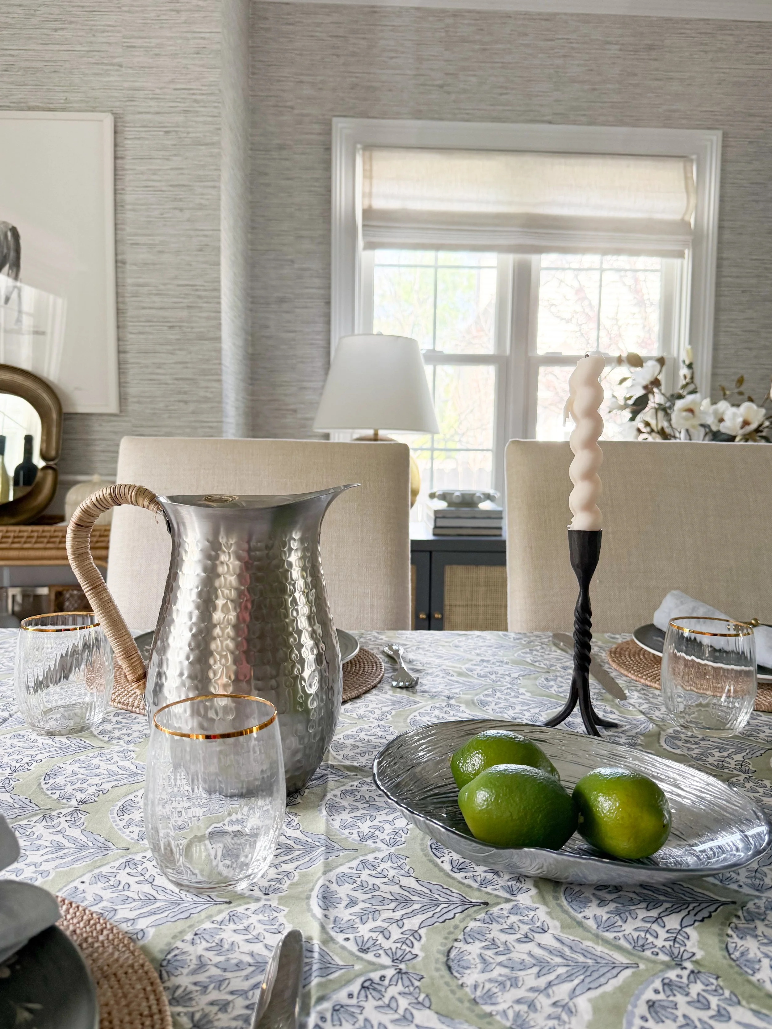 McGee and Co tablescape detail with hammered metal pitcher, fresh limes, textured glassware, and candles for a warm layered look