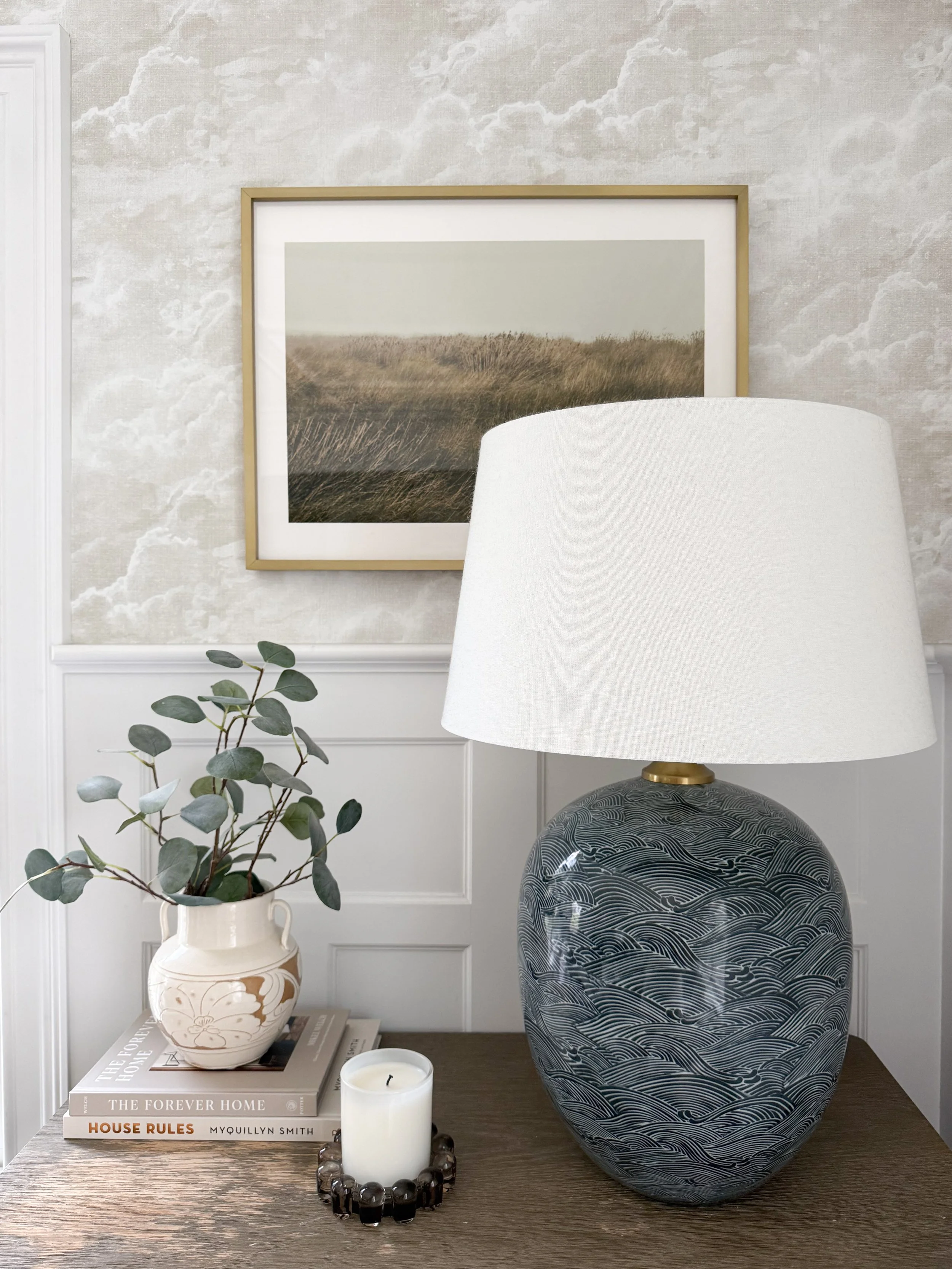 Large ceramic table lamp with a white linen shade styled on a living room side table beside neutral artwork.