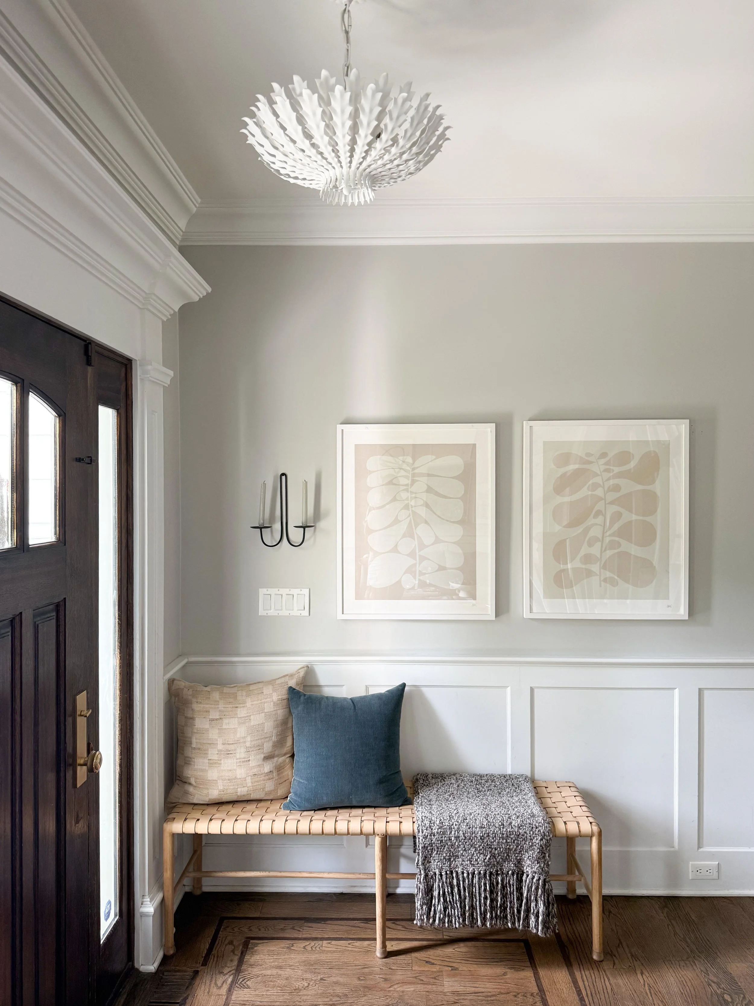 Modern entryway with a sculptural white ceiling light fixture, woven bench, wall sconces, and neutral home decor.