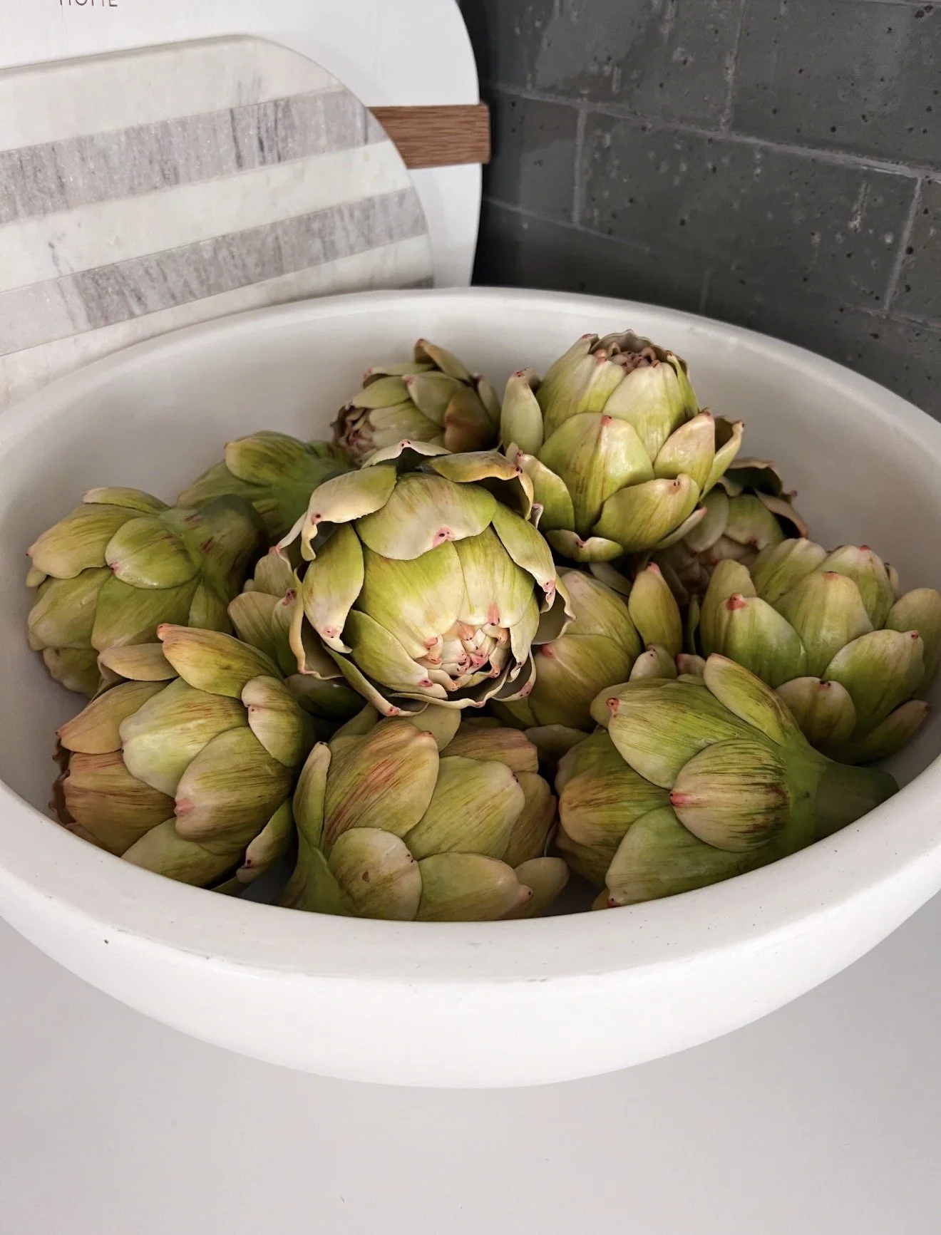 Faux artichokes styled in oversized white decorative bowl for organic neutral kitchen and coffee table decor inspiration
