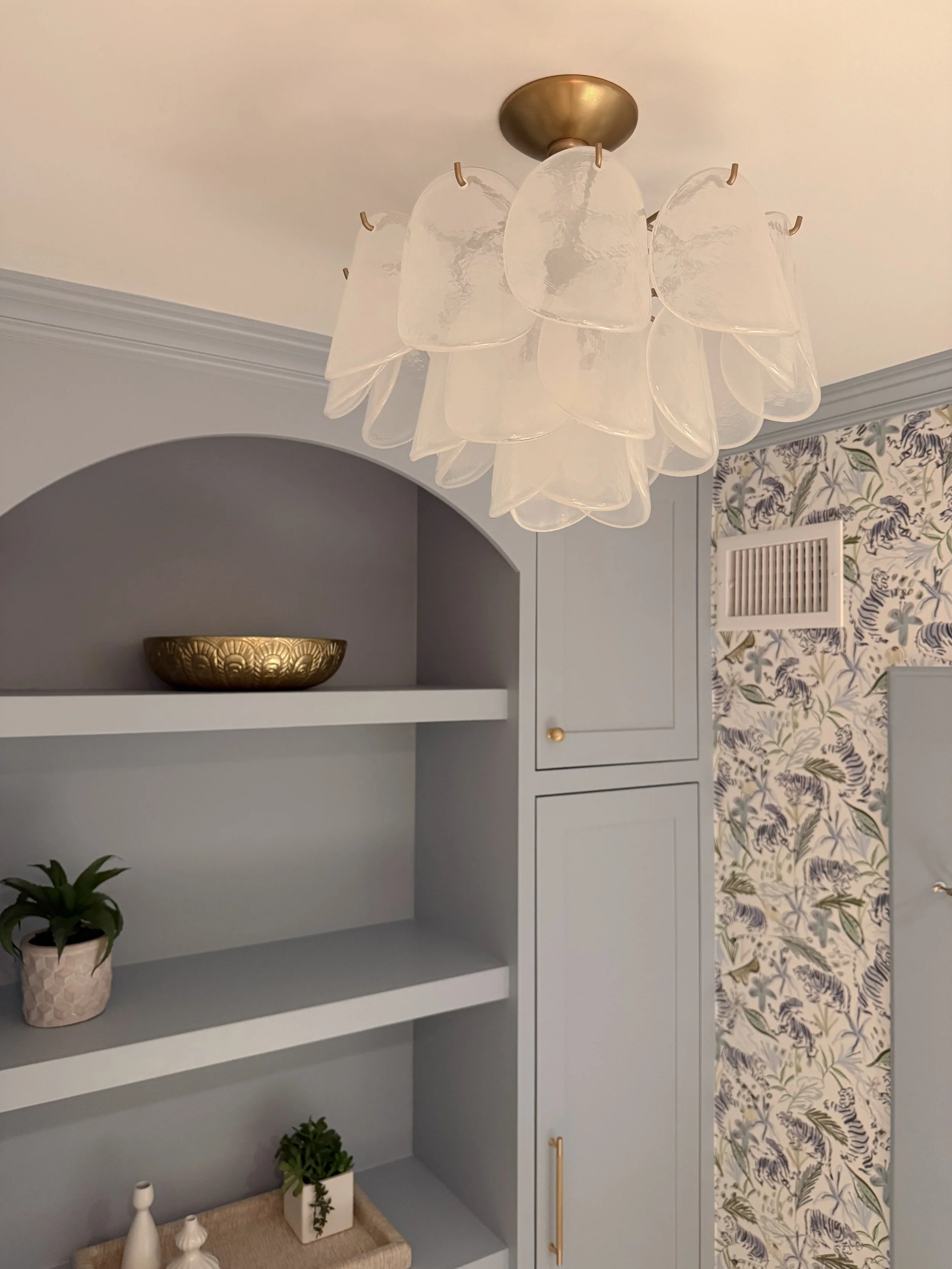 Blue built in powder room cabinetry with open shelves, tiger wallpaper and a decorative semi flushmount light.