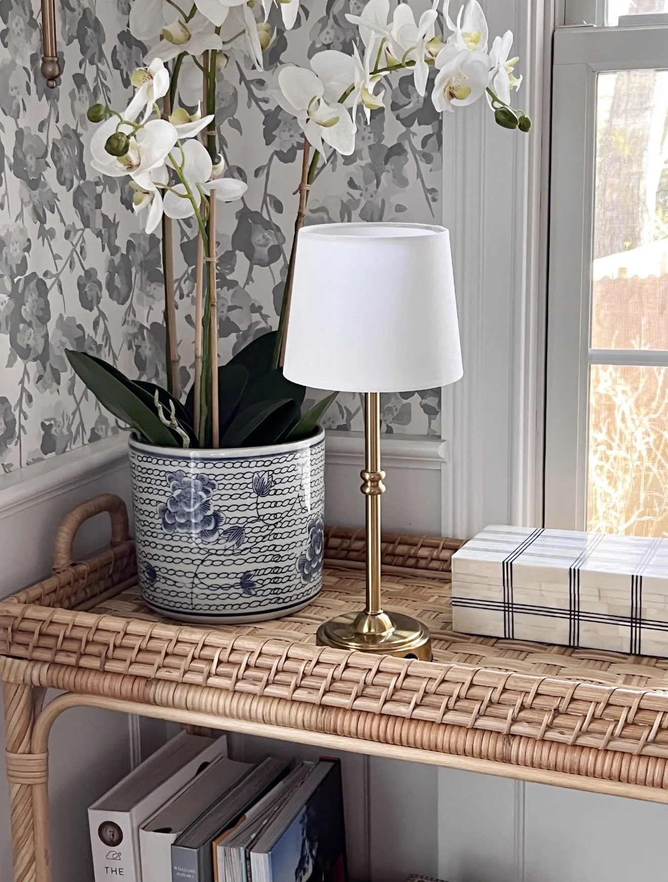 Brass cordless table lamp styled on woven console table beside orchid planter and decorative storage boxes in cozy neutral home