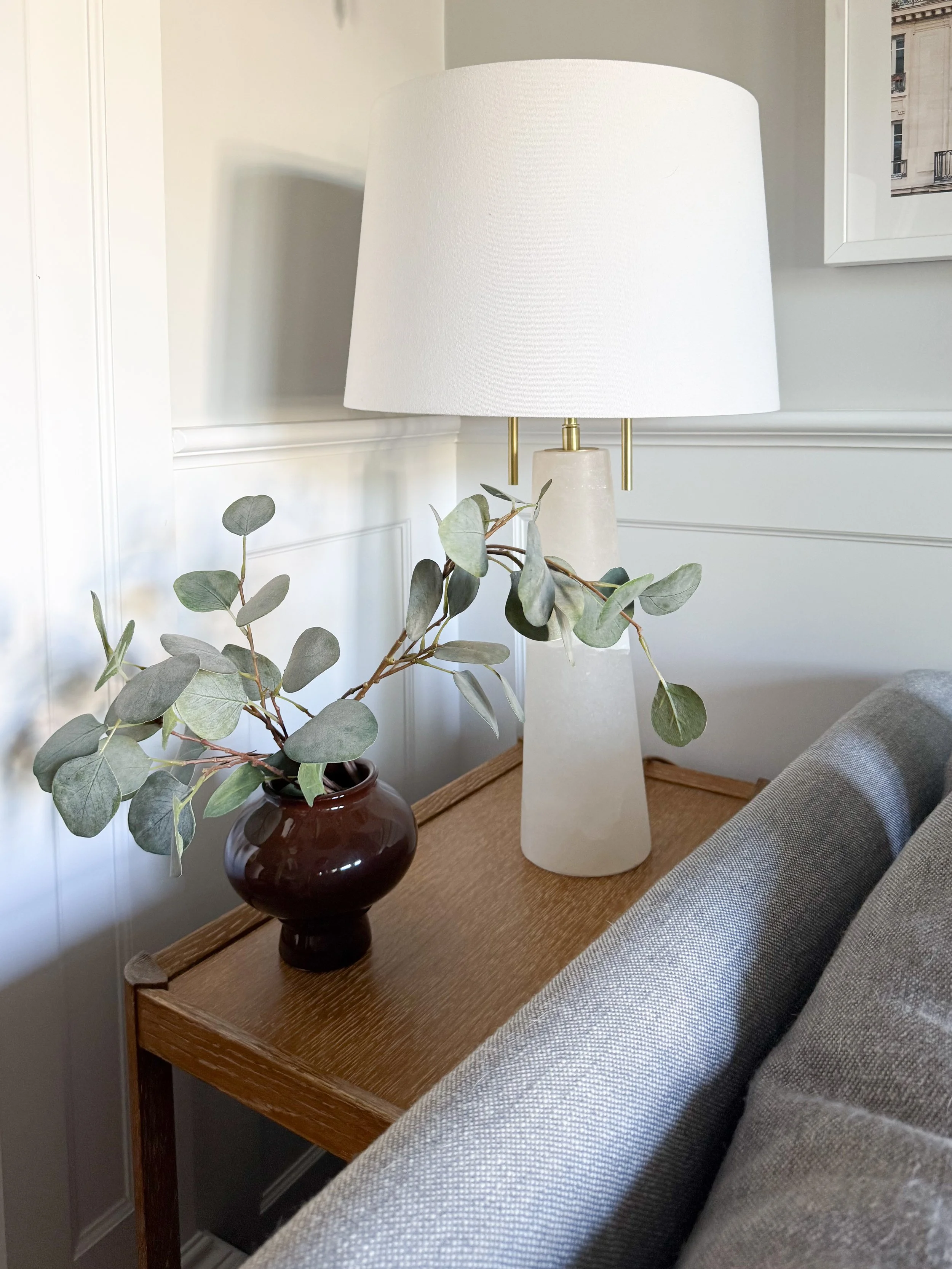 Decorative table lamp styled on a wood side table with framed artwork and home accents in a bright transitional living room.