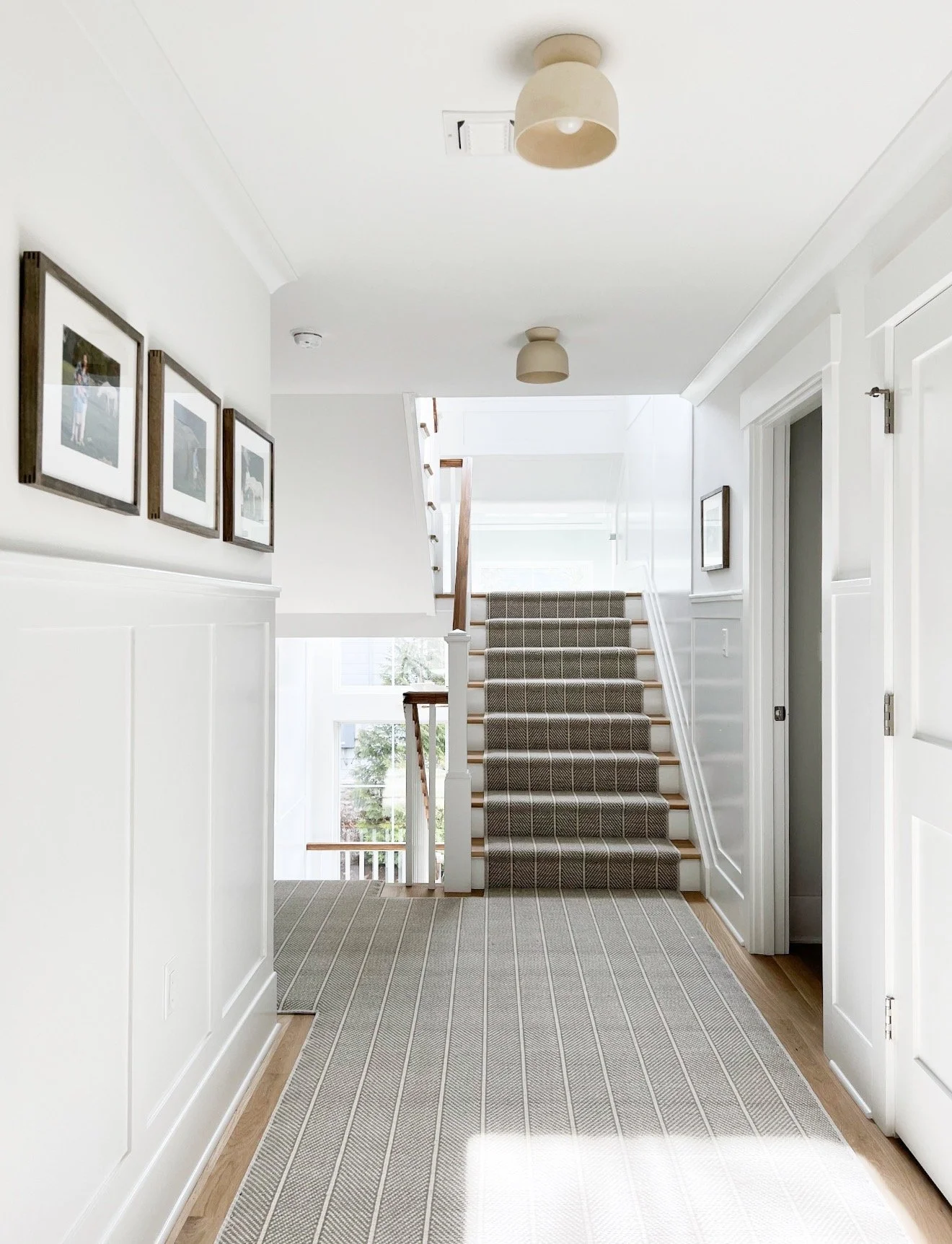 Open stairwell featuring oversized woven pendant lights, white railings, natural wood accents, and large windows