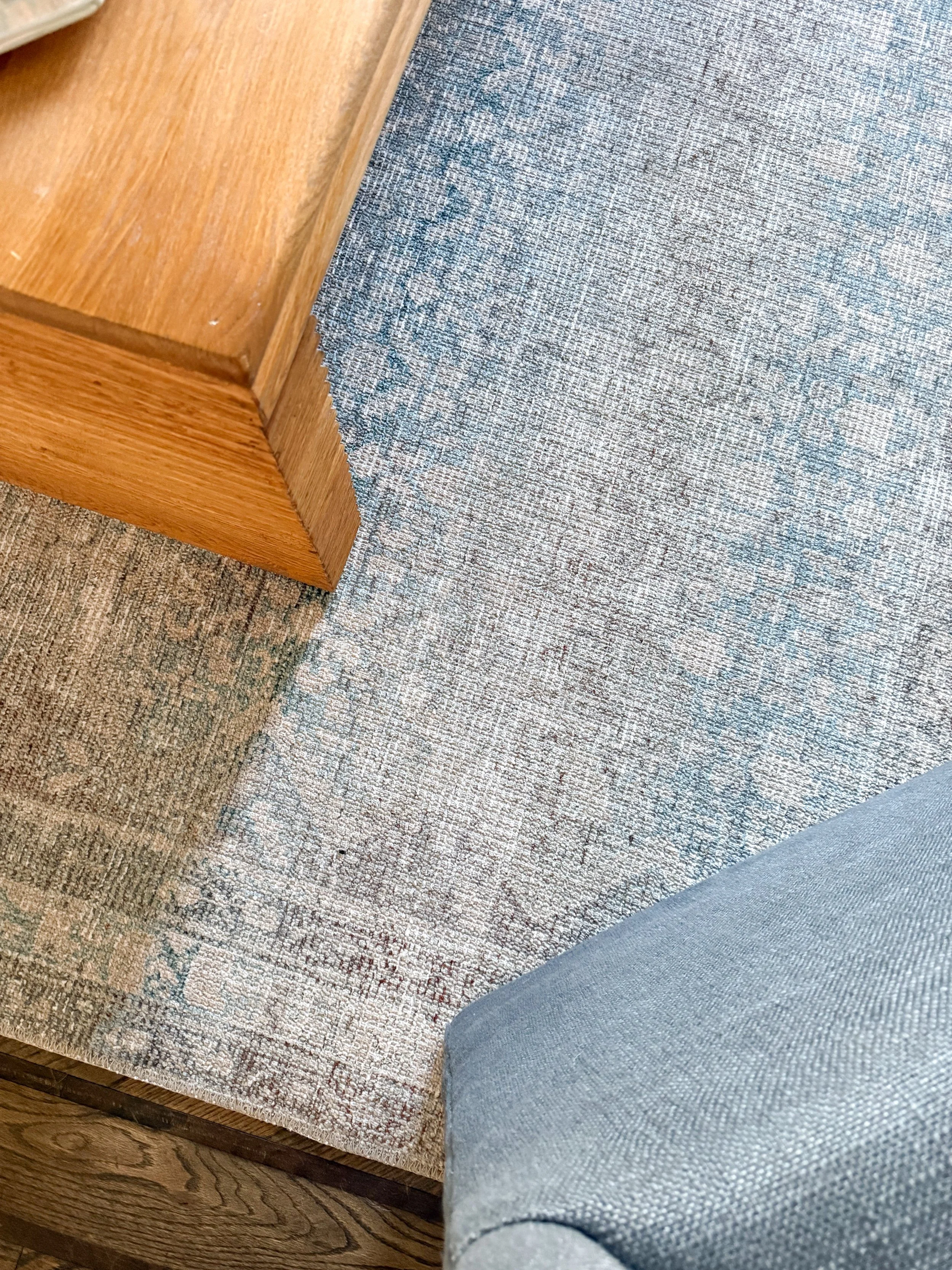 Close up of a vintage inspired blue and cream area rug layered beneath a wood coffee table in a beautifully styled living room.