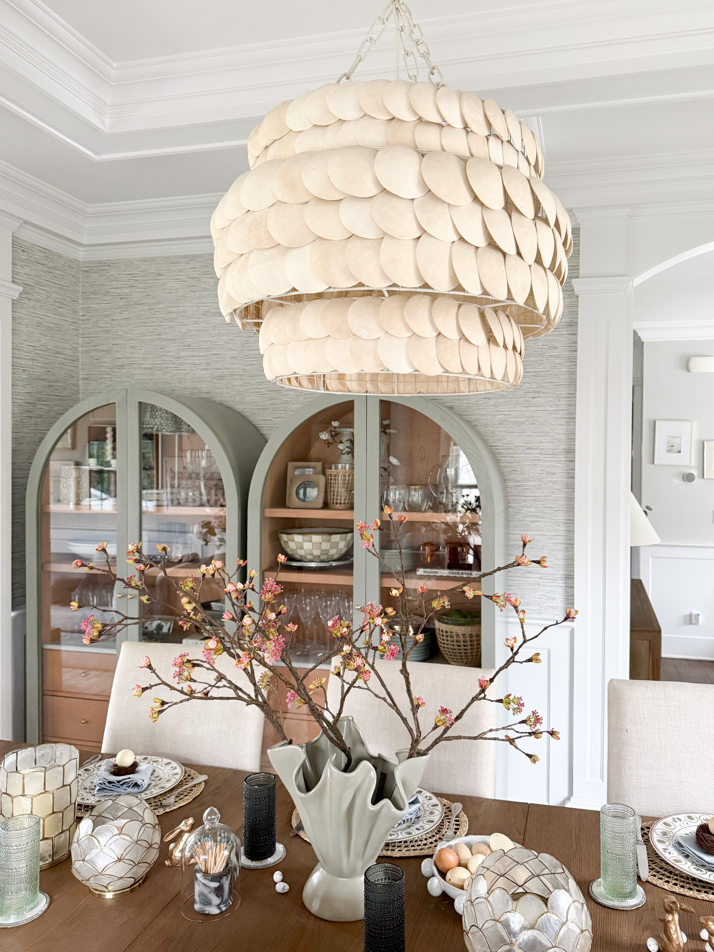 Spring table centerpiece with floral branches in ceramic vase, neutral Easter decor, glass candle holders, and woven placemats