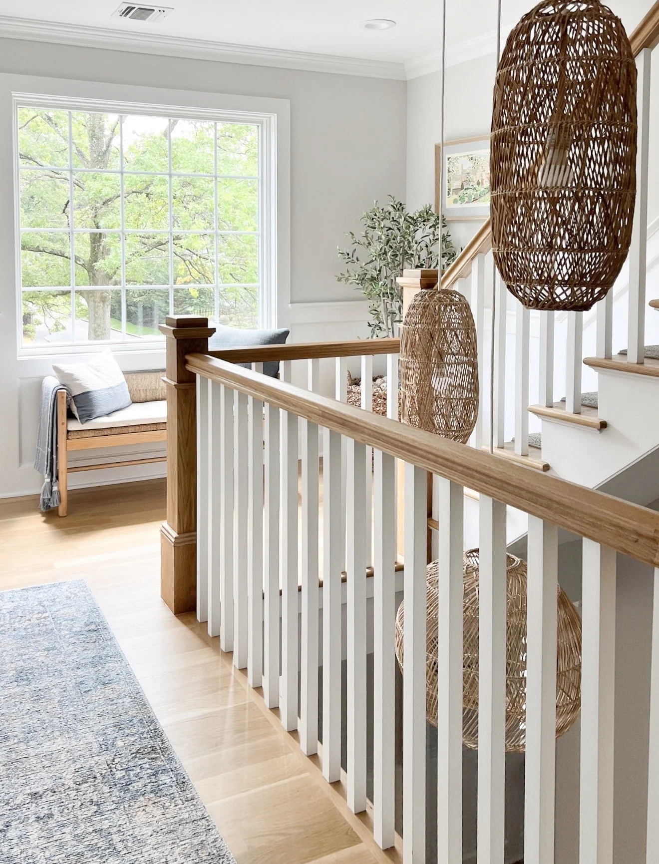 Open stairwell featuring oversized woven pendant lights, white railings, natural wood accents, and large windows.