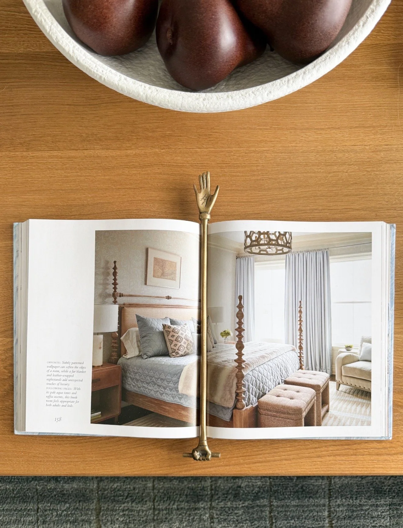 Decorative brass hand bookmark styled on open coffee table design book in cozy neutral living room with layered styling details