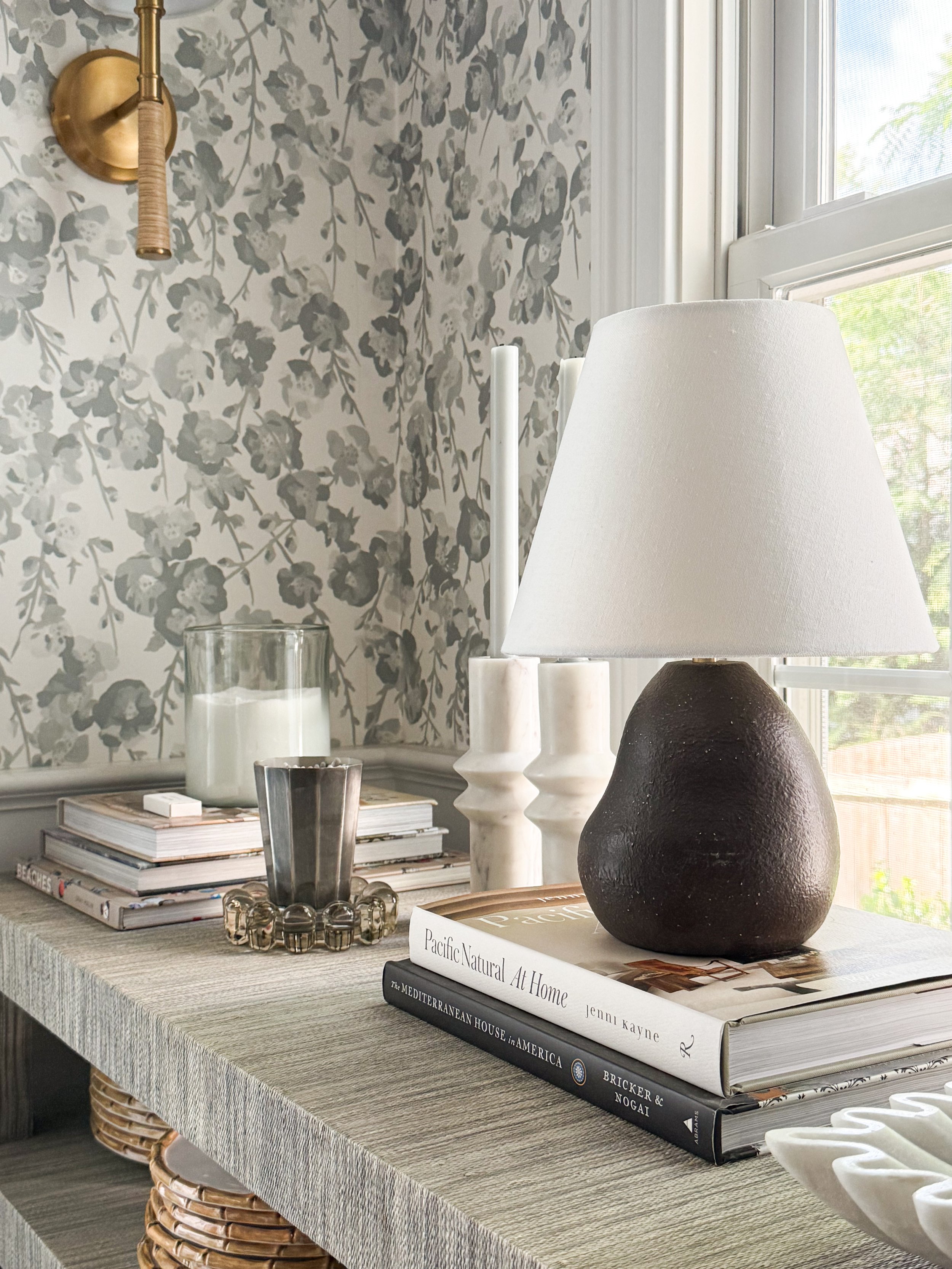 Dark ceramic table lamp with a white linen shade styled on a breakfast nook console beneath floral wallpaper.