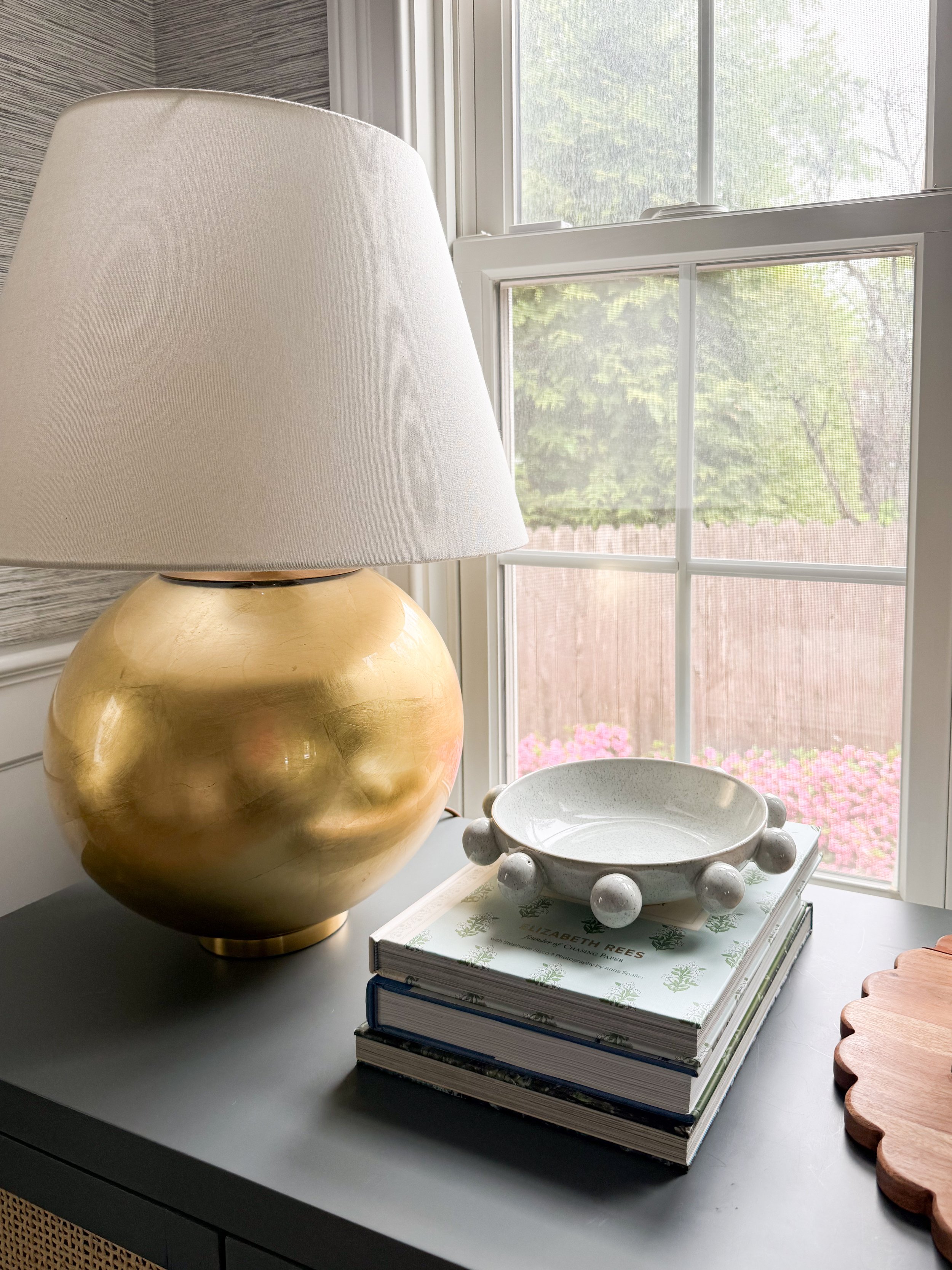 Neutral ceramic decorative dish styled on stacked coffee table books beside marble lamp and layered traditional home decor accessories