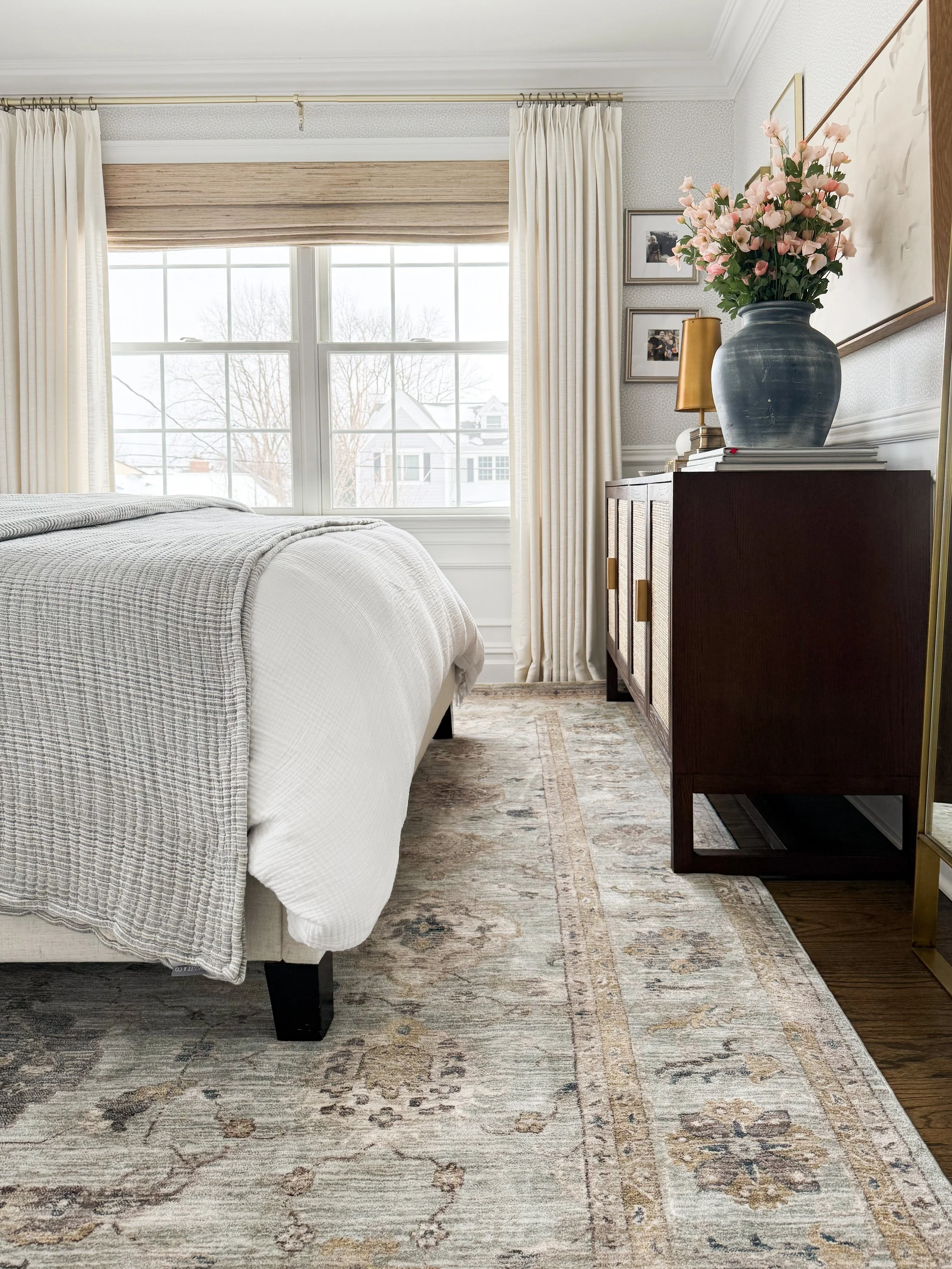 Neutral primary bedroom with a king bed, light patterned area rug, wood nightstands, and cozy bedding.