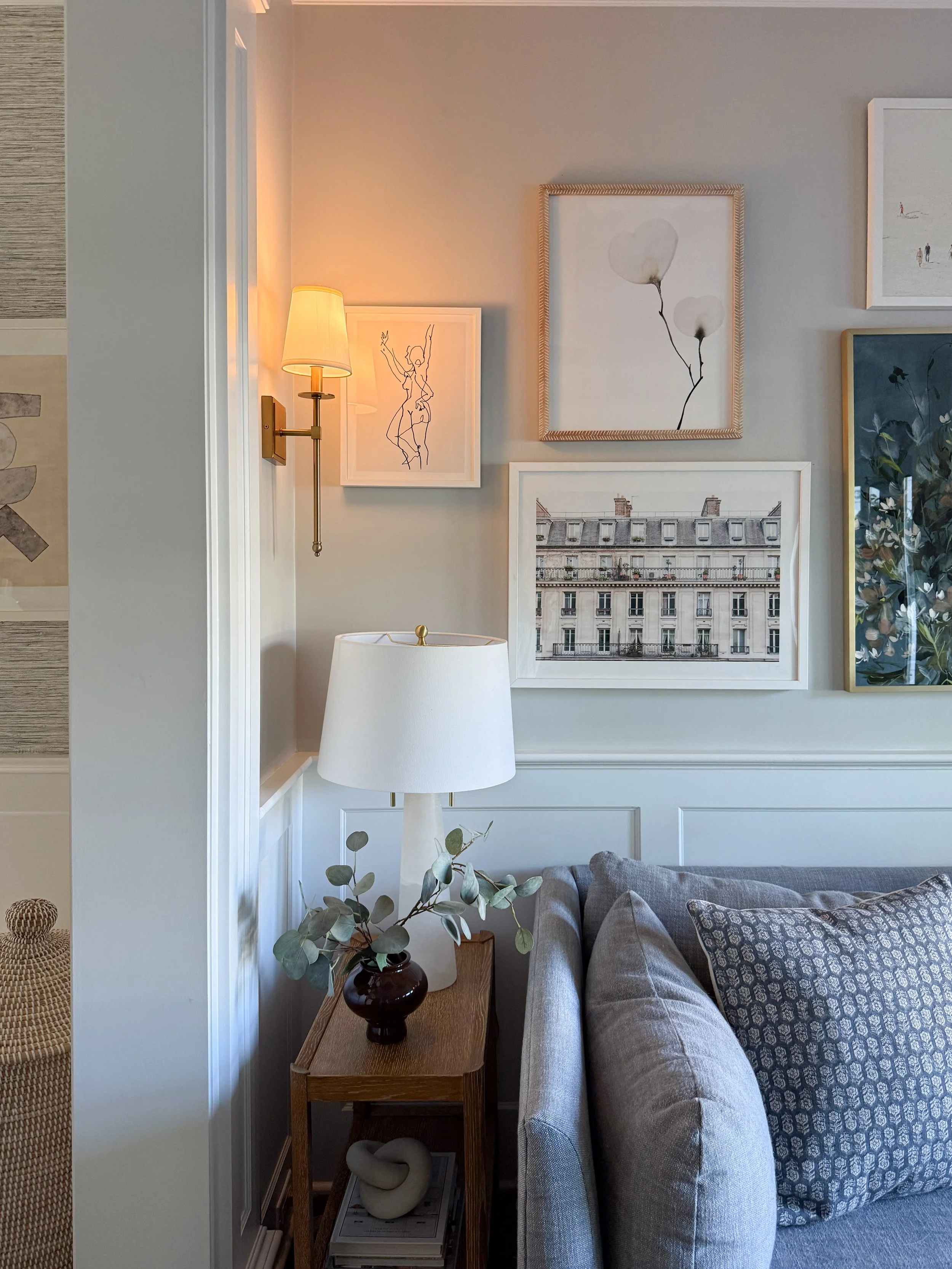Curated gallery wall featuring framed artwork, photography, and sketches arranged above a neutral sofa in a sophisticated living room.