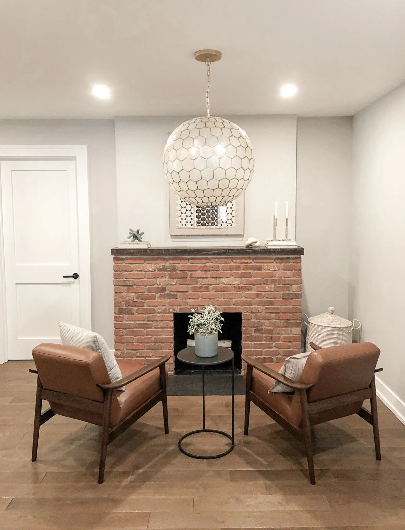Sitting area with leather accent chairs, exposed brick fireplace, and oversized capiz shell globe pendant light.